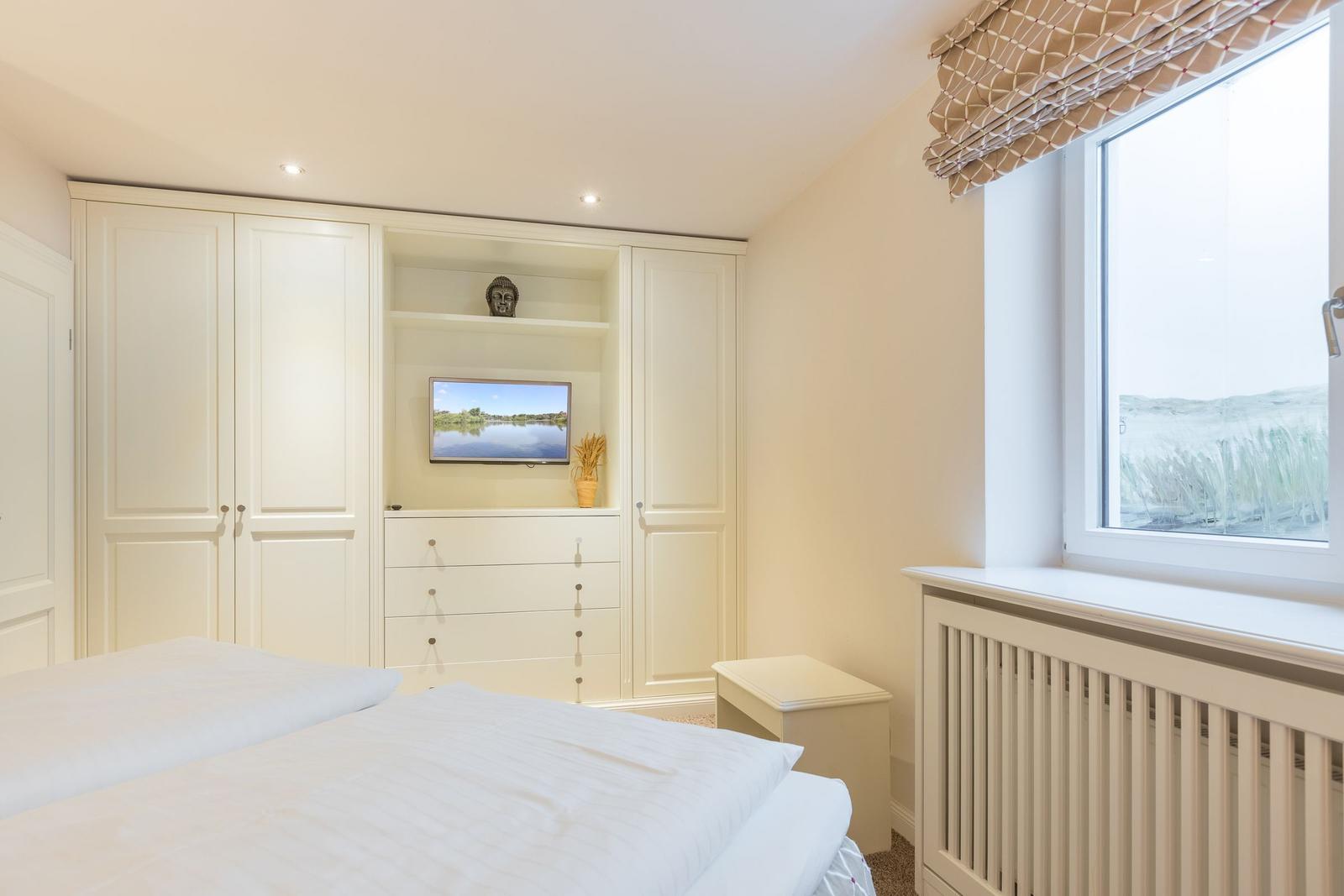 Schlafzimmer mit weißem Schrank, Fernseher und Fenster mit Blick auf Gras.