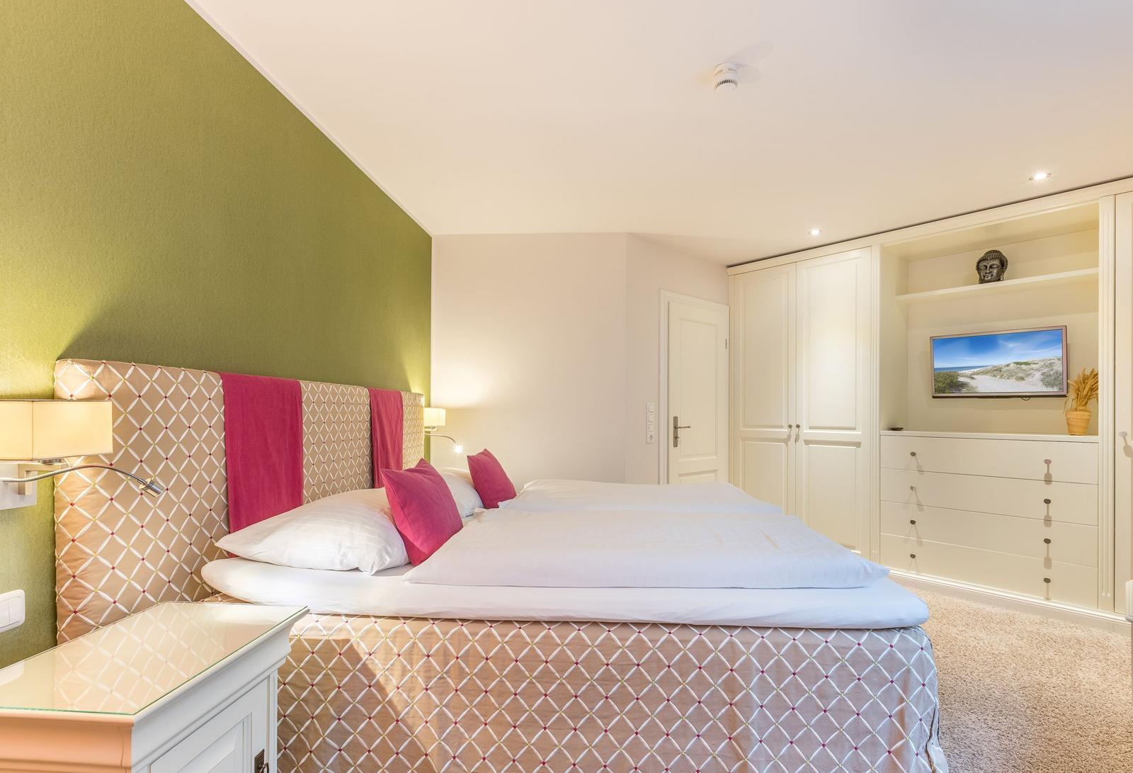 Schlafzimmer mit Doppelbett, grüner Wand und integriertem Schrank mit TV.