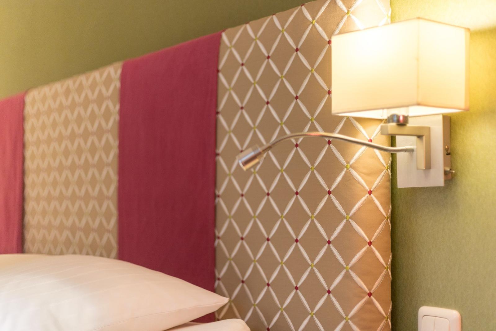 Bettkopfteil mit gemustertem Stoff und Wandlampe