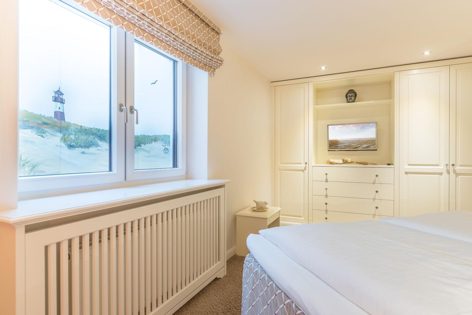 Schlafzimmer mit Blick auf Leuchtturm, weißes Bett und Einbauschränke.