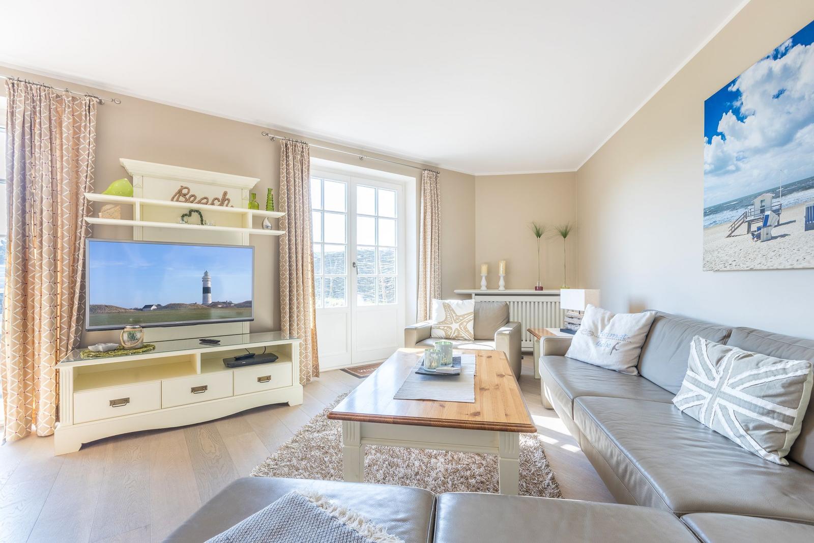 Wohnzimmer mit Sofa, Couchtisch und Fernseher. Fenster mit Blick aufs Meer.