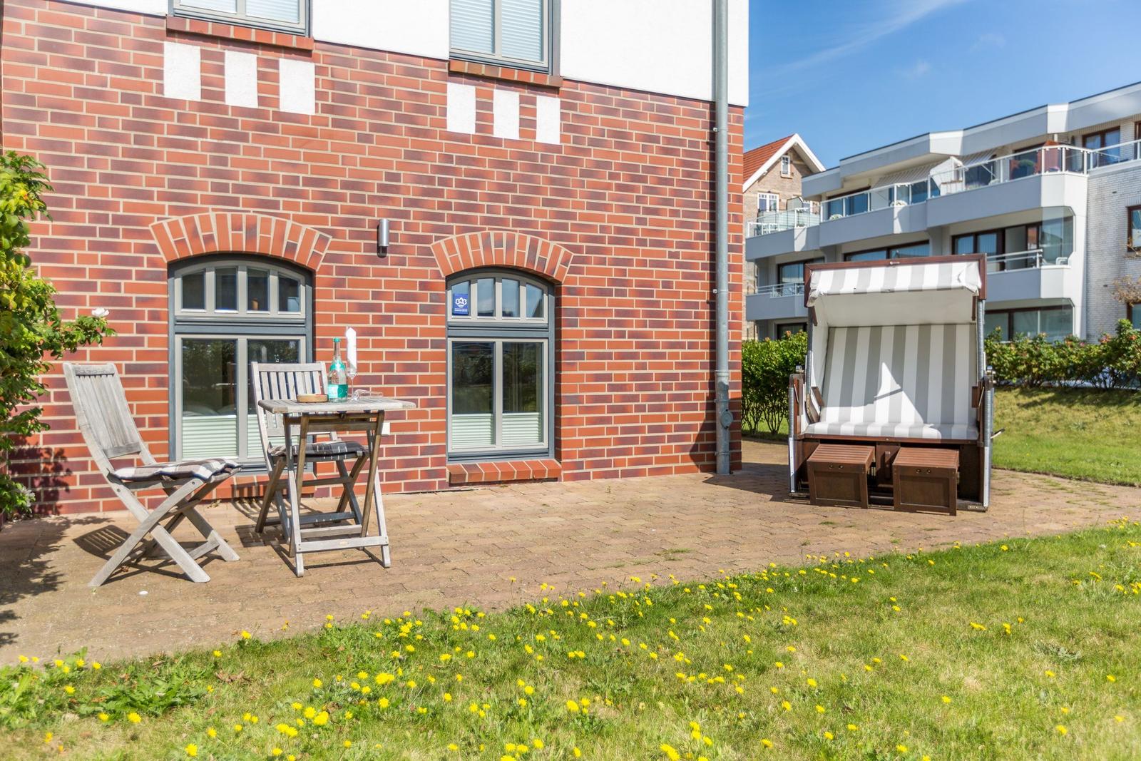 Terrace with table, chairs, and beach chair in front of red brick house.