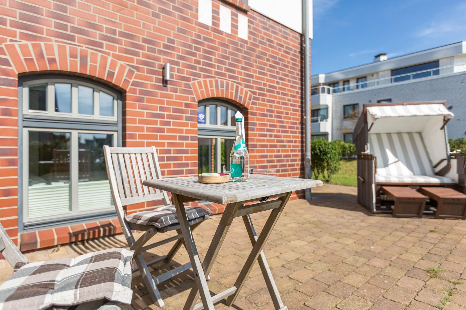Terrace with table, chairs, and lounge chair in front of red brick house.