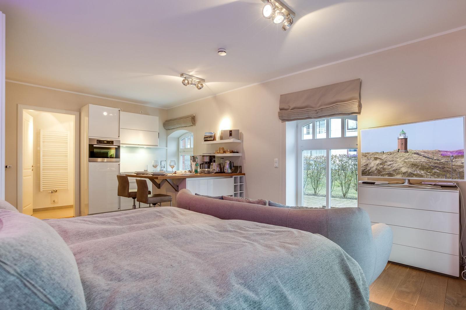 Bedroom with kitchen area and TV. Large windows and modern furniture.