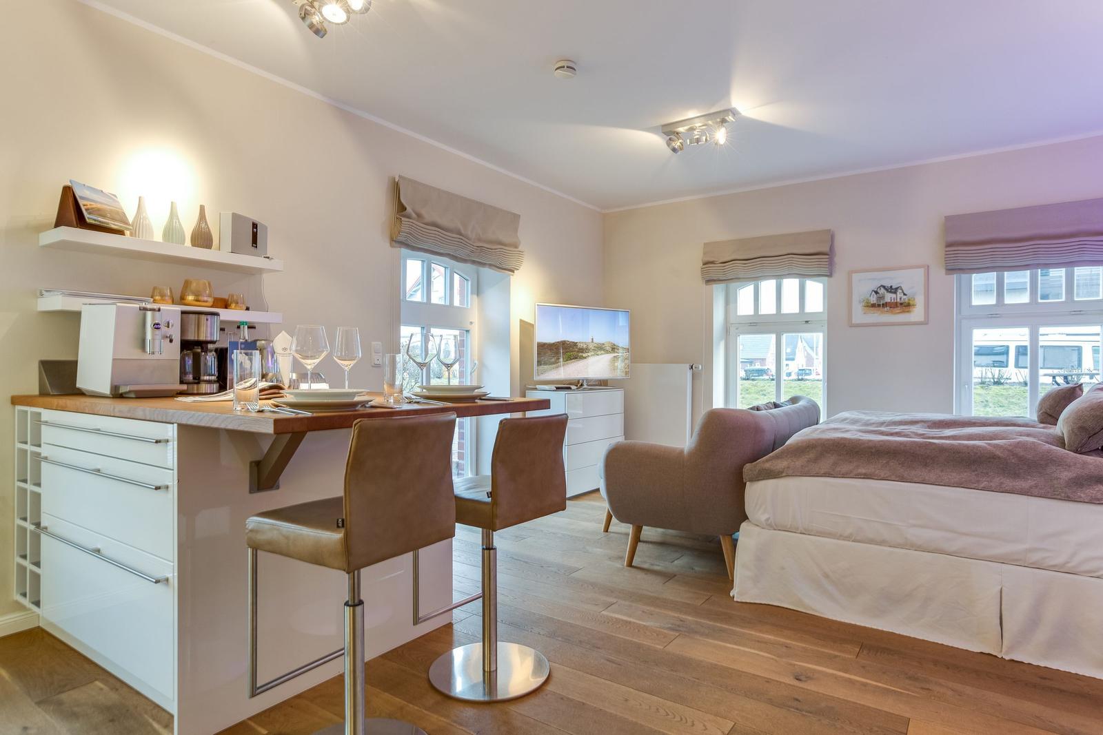 Bedroom with kitchen area and TV. Wooden floor and large windows.