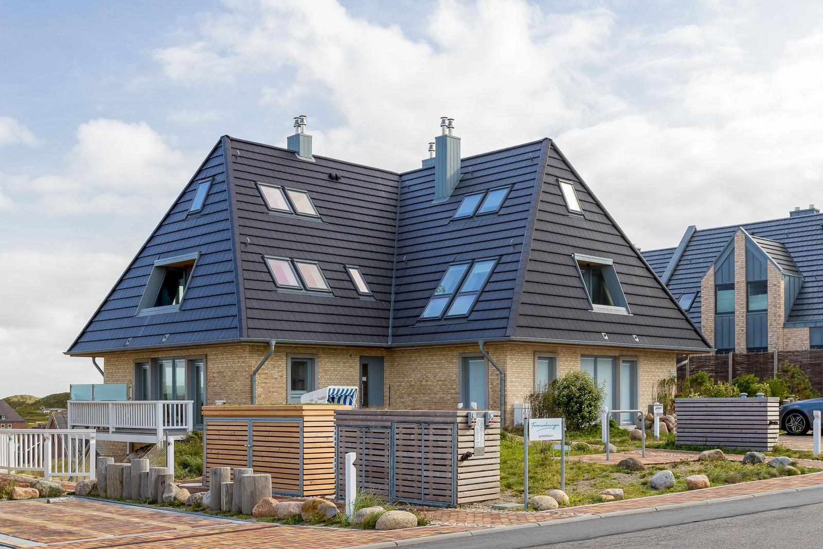 Modernes Haus mit dunklem Dach und Holzfassade. Terrasse und Gartenbereich.
