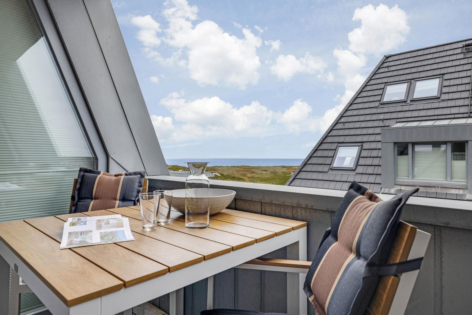 Terrasse mit Tisch und Stühlen. Blick auf Meer und Himmel.