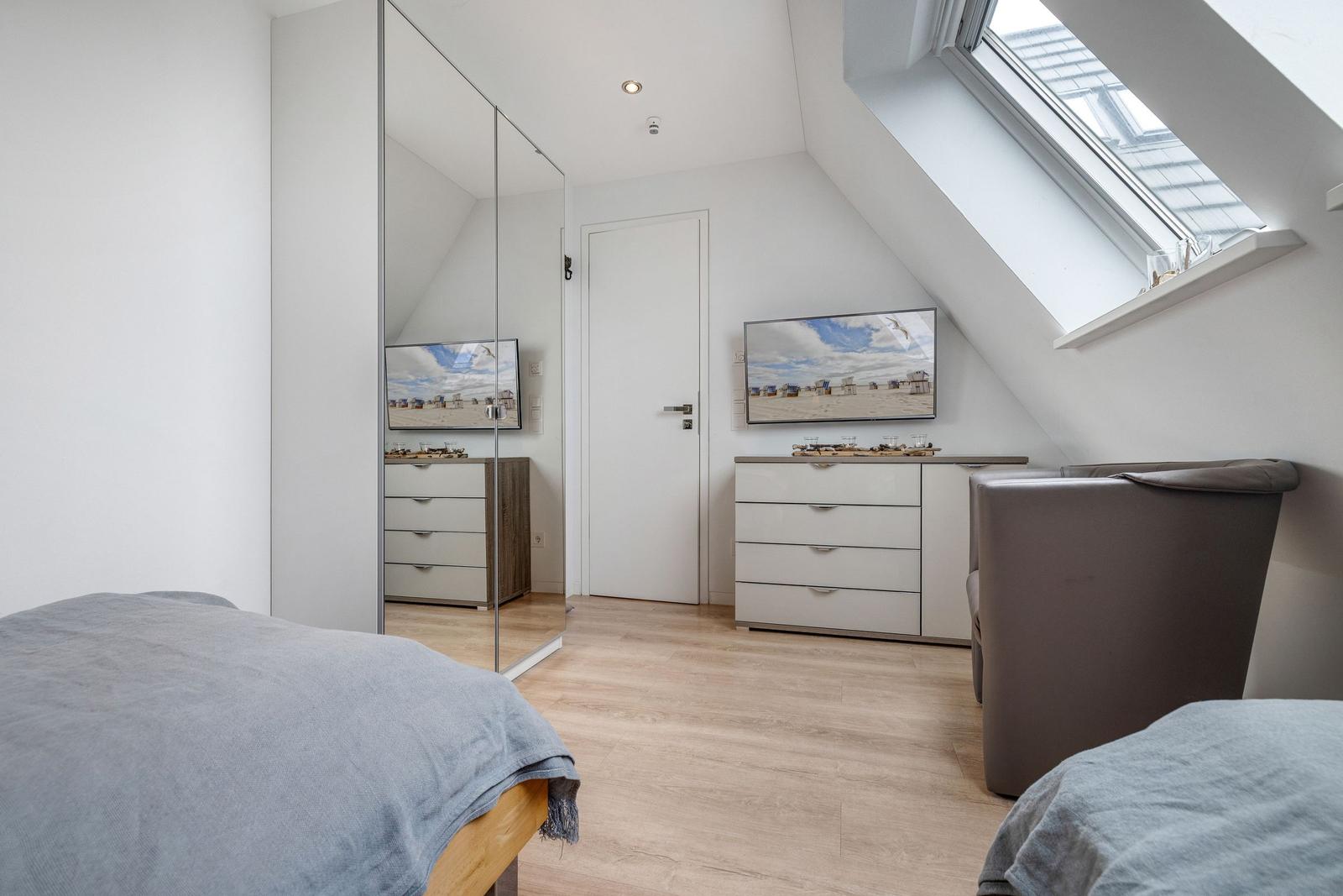 Schlafzimmer mit Dachschrägen, Fenster, Kleiderschrank und Bett.