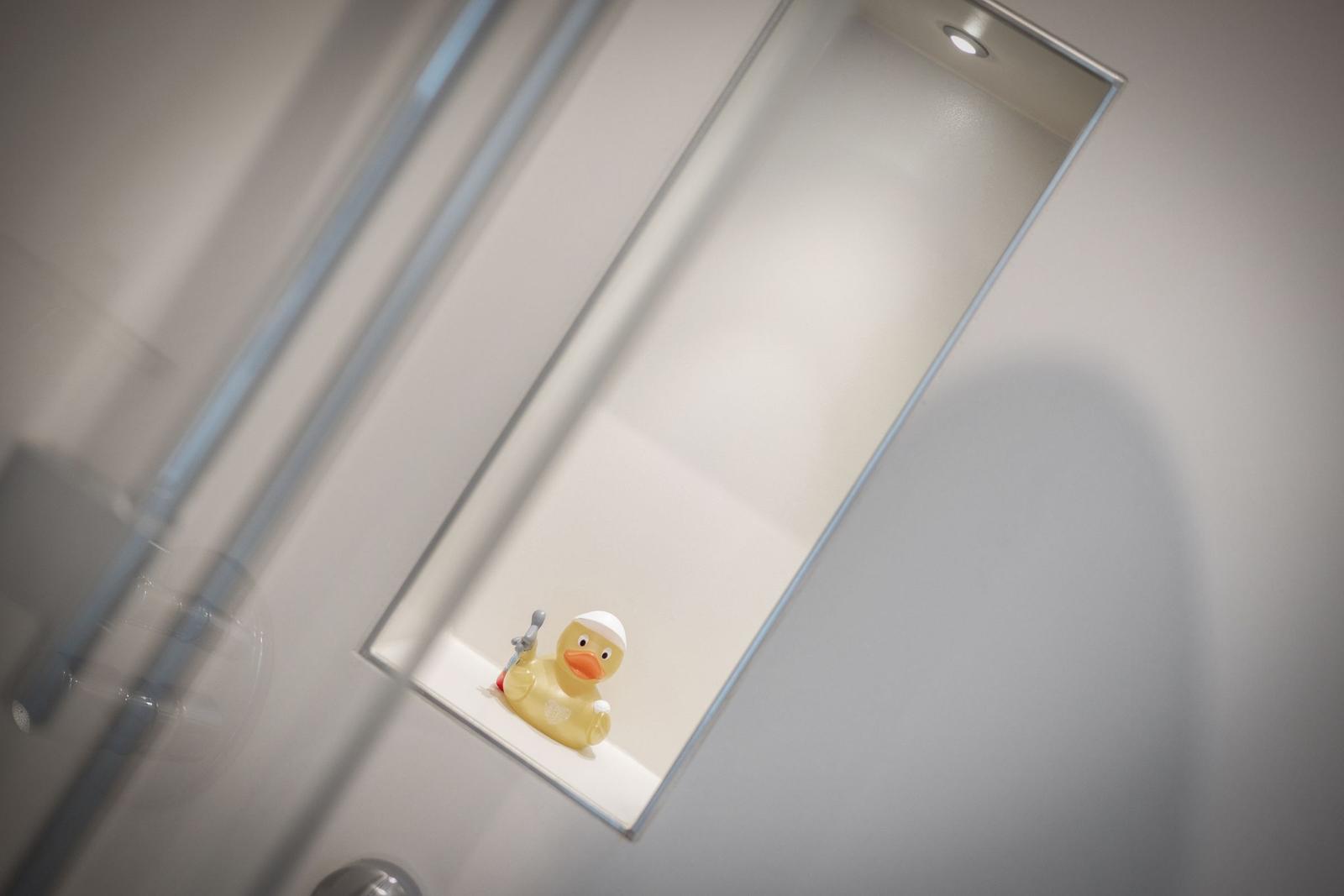 Ein gelbes Schwimmpfuhlchen mit Schutzkappe sitzt in einem Duschbereich.