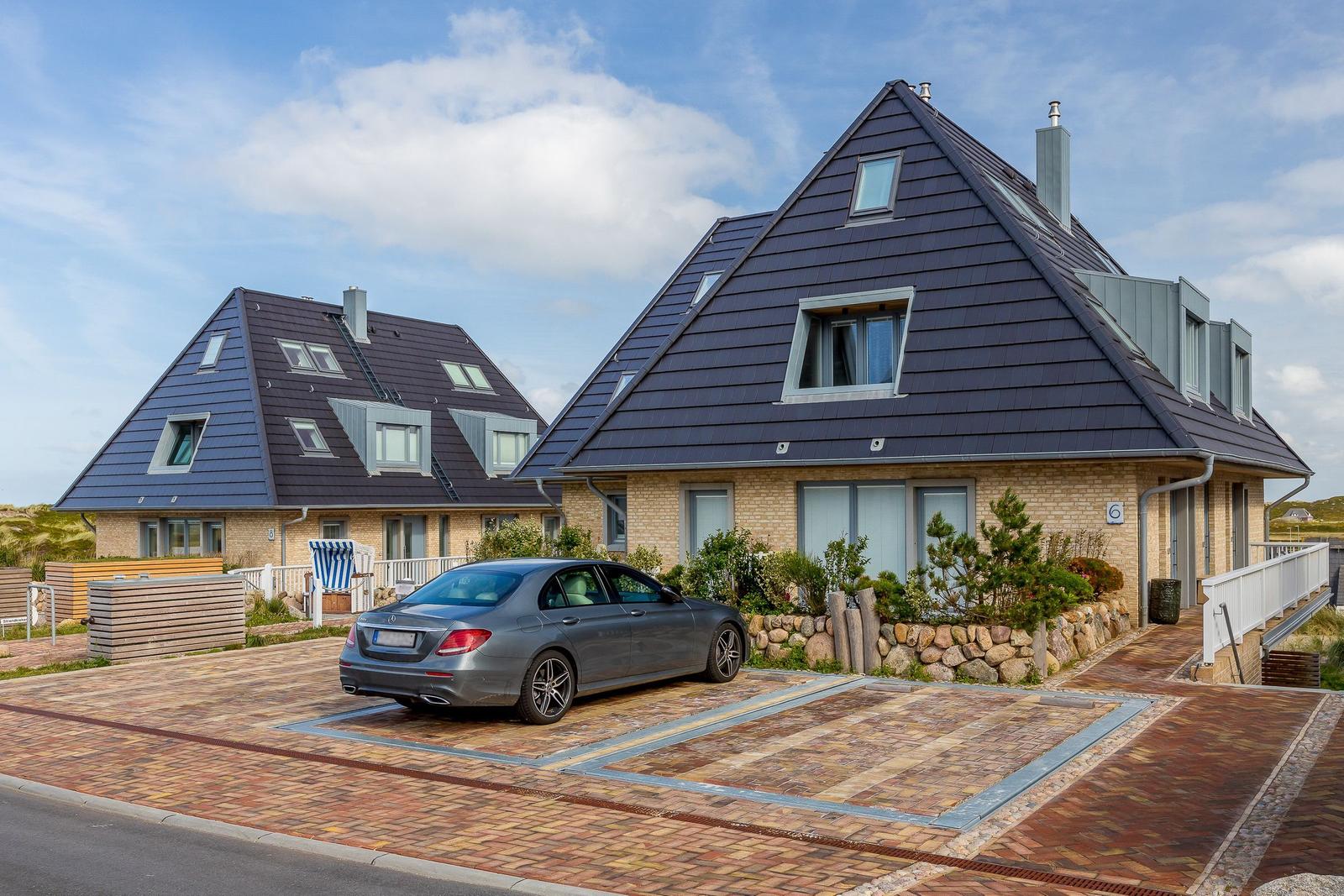 Moderne Ferienhaus mit dunklem Dach und gepflastertem Hof. Ein Auto parkt auf dem Hof.