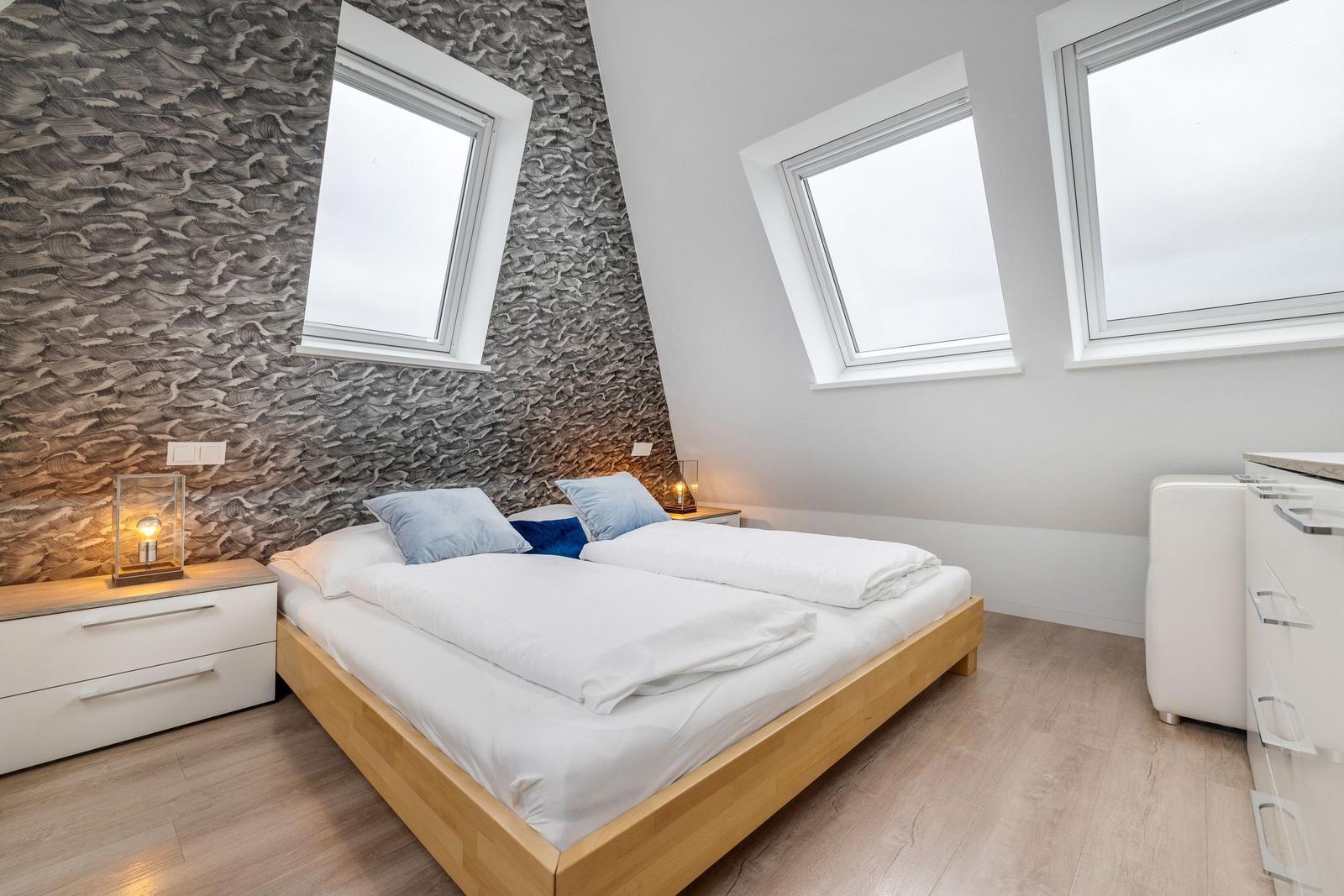 Schlafzimmer mit Doppelbett, zwei Fenstern und Textilwand