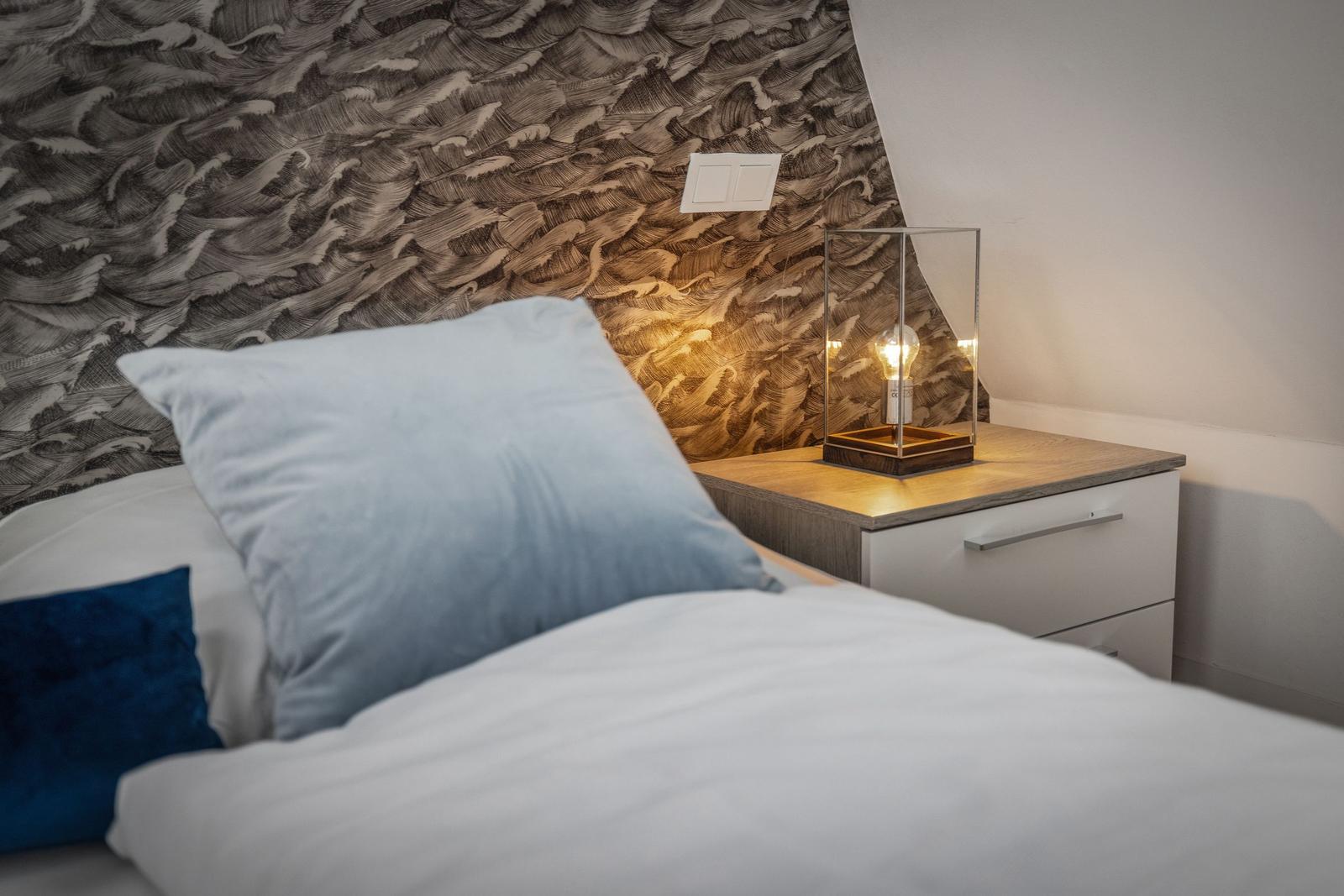 Schlafzimmer mit Bett, Nachttisch und Wandtapete mit Wellenmuster.
