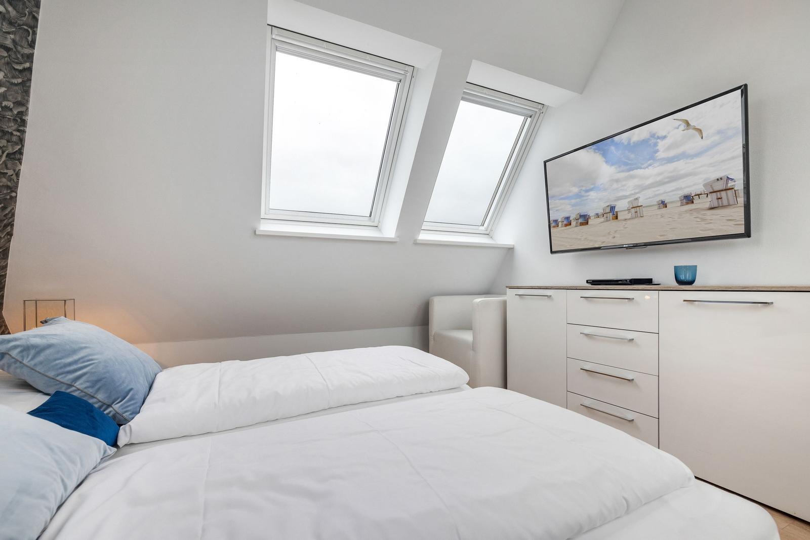 Schlafzimmer mit Dachfenstern, Bett, TV und Schrank.