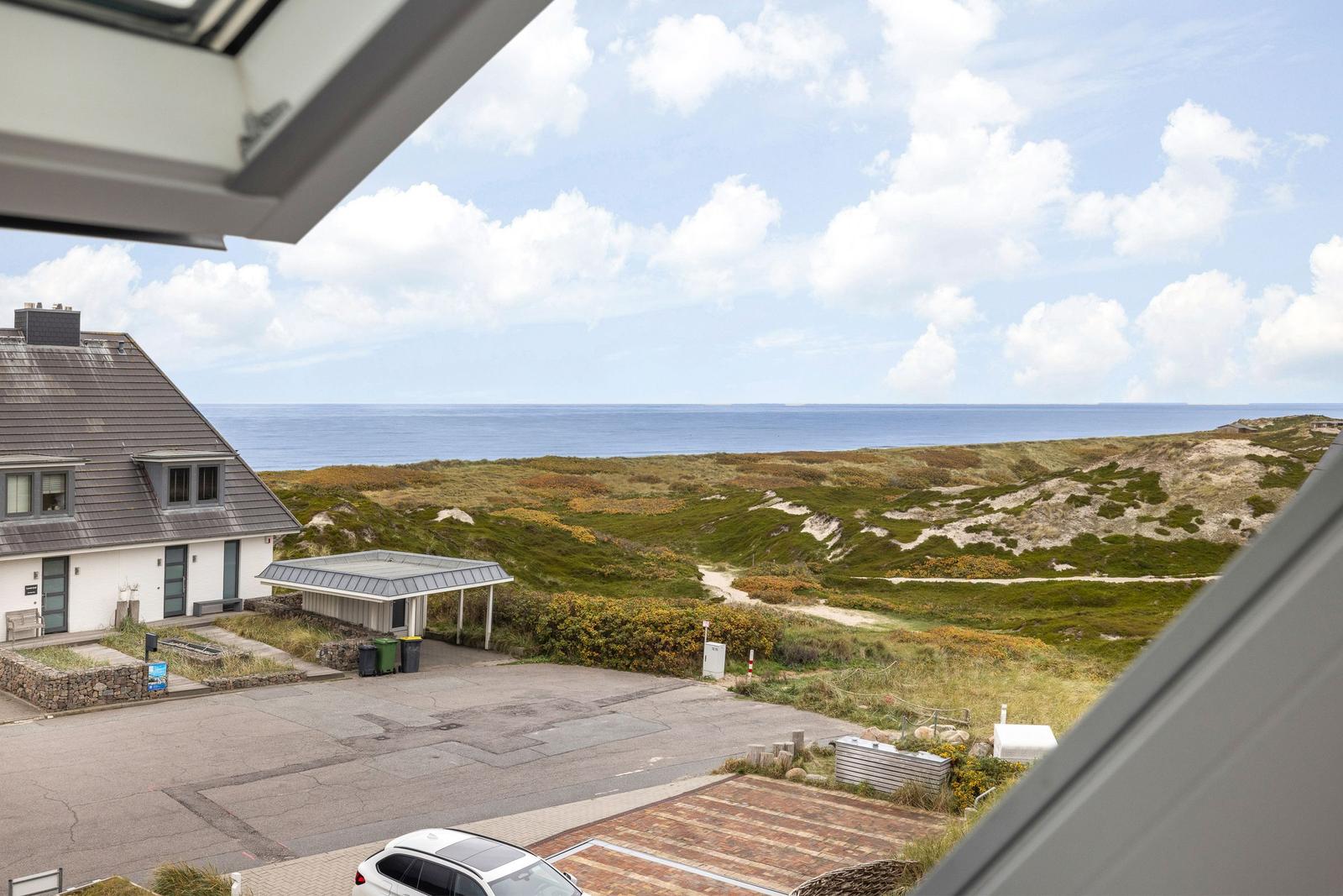 Meerblick von einem Fenster, mit Strand und Dünen im Vordergrund.