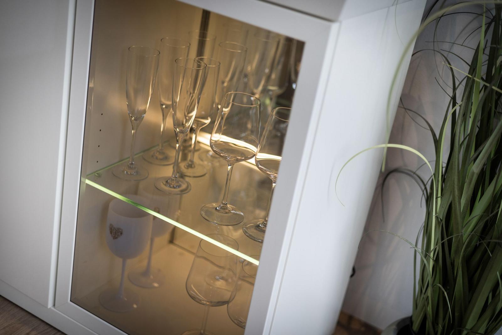 Wein- und Champagnergläser im beleuchteten Schrank neben einer Pflanze.