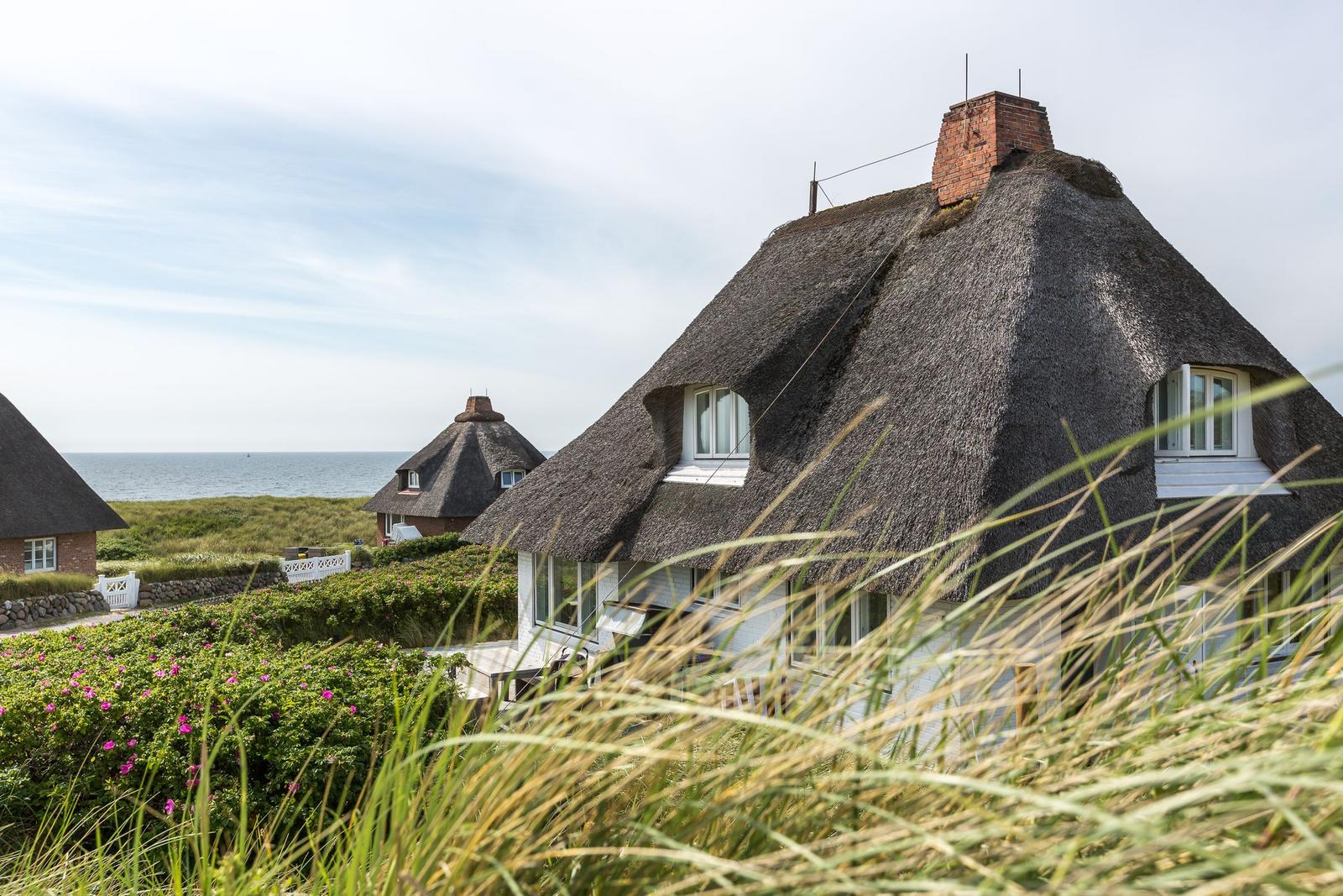 Dorfhaus mit Strohdach und Meerblick durch Gräser