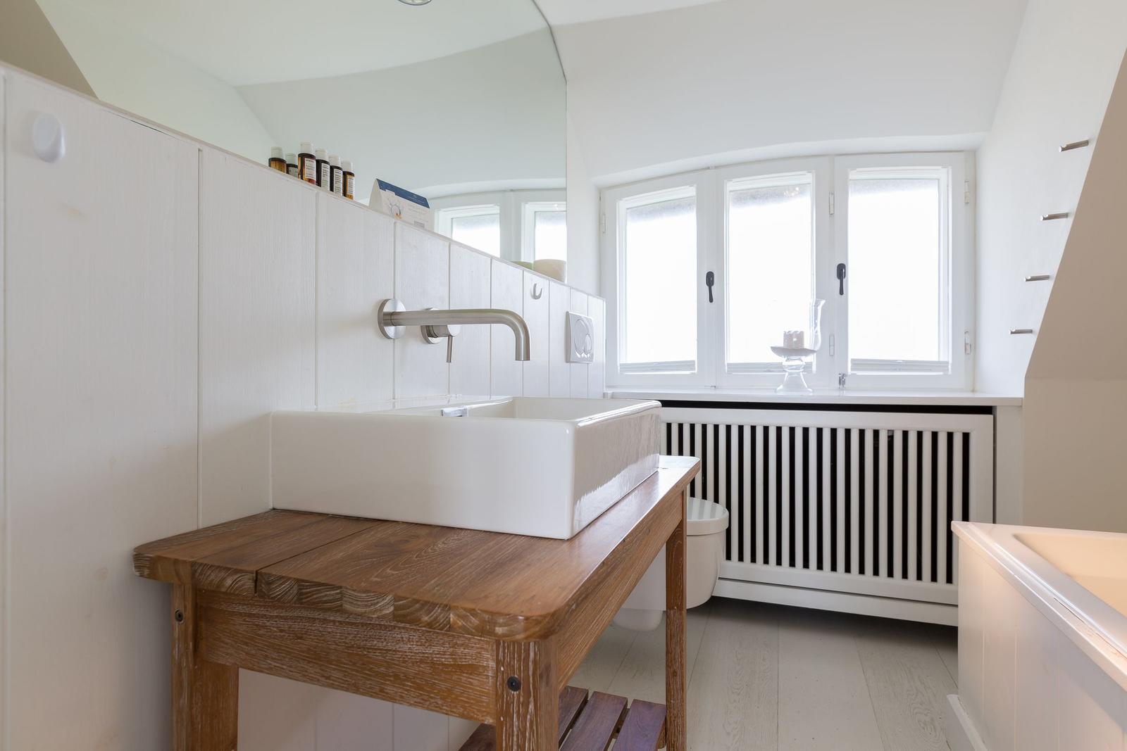 Badezimmer mit Waschtisch auf Holzbank, Fenster und Heizkörper.