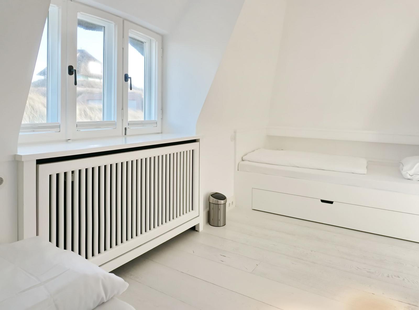 Schlafzimmer mit weißem Bett, Fenster und Heizkörper