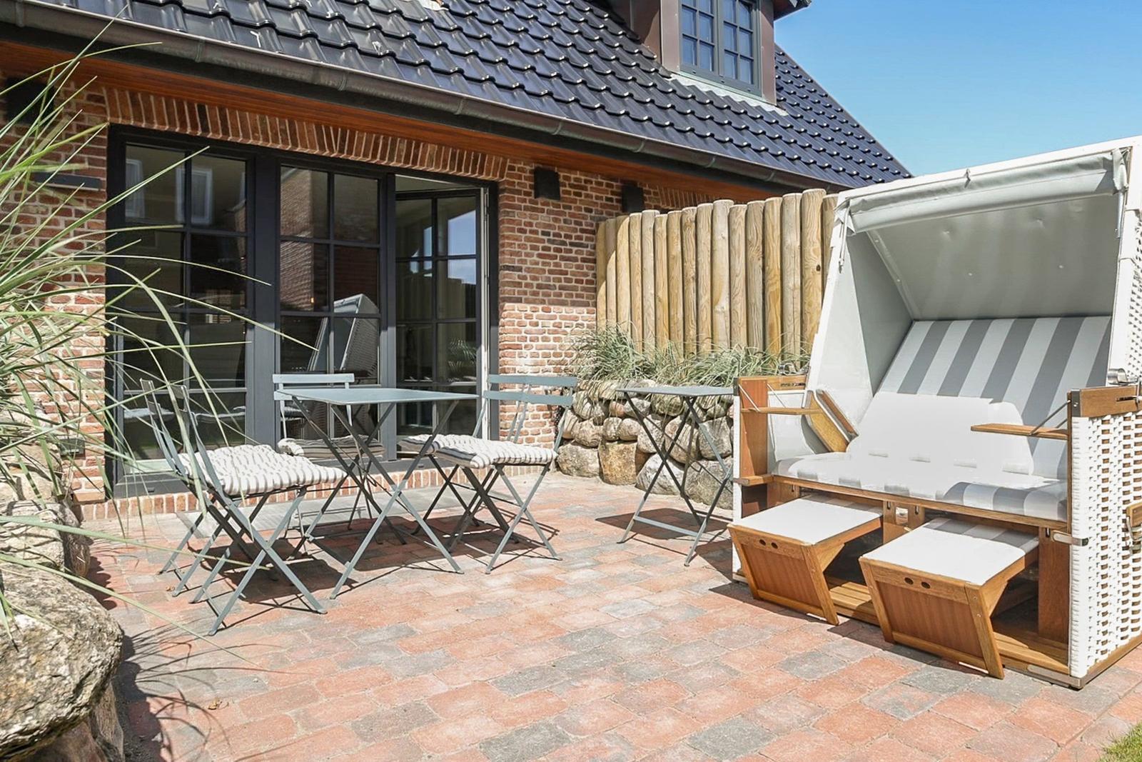Terrasse mit Tisch, Stühlen und Strandkorb auf Steinplatten.