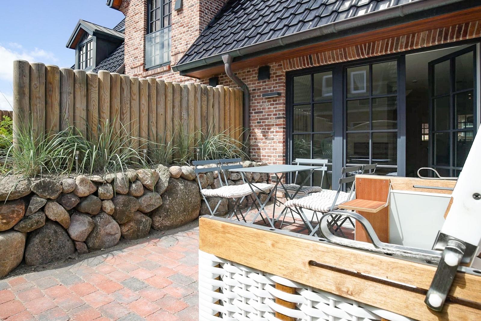 Terrasse mit Tisch, Stühlen und Steinmauer. Hinterhof mit Holzzaun und Backsteinhaus.