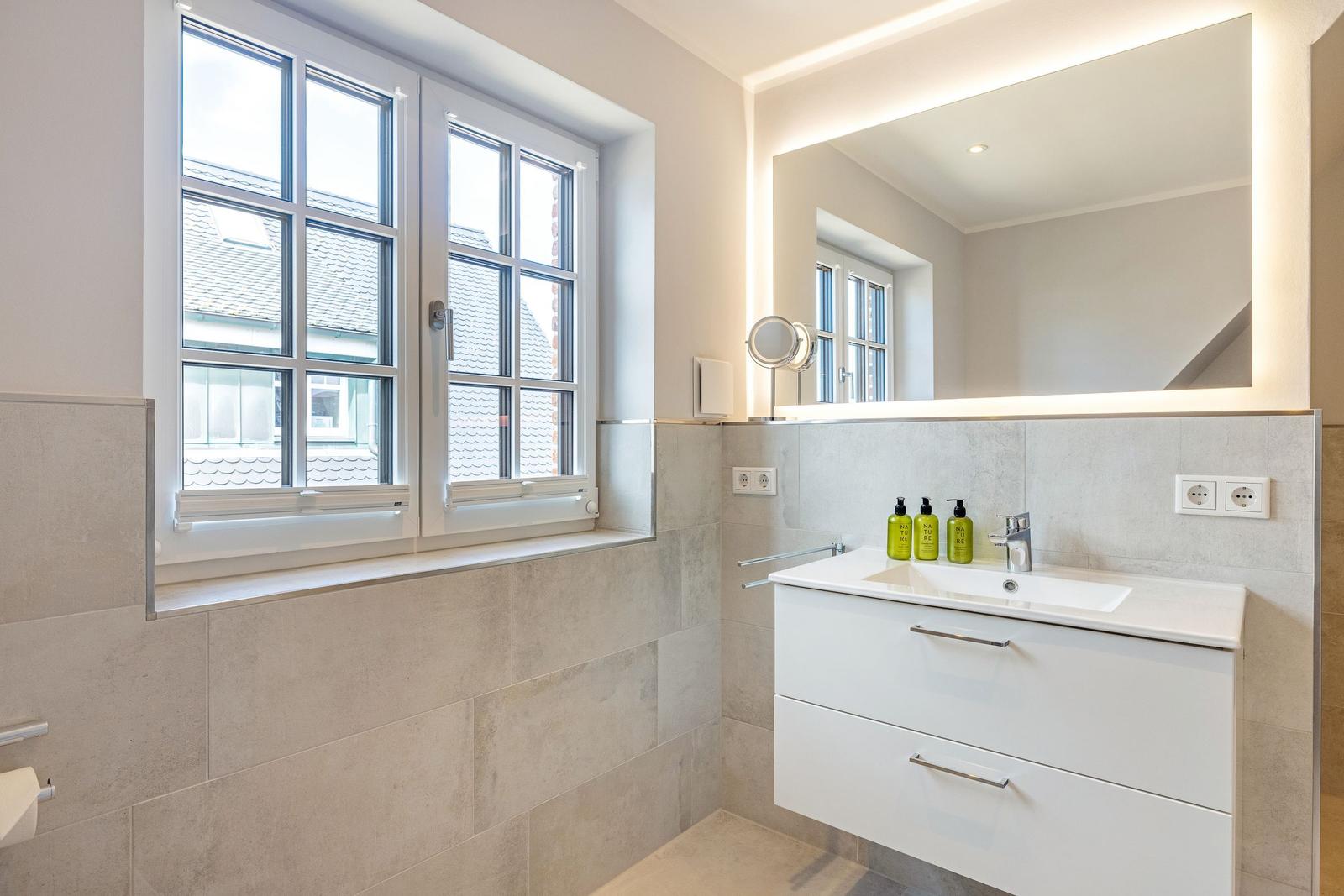 Badezimmer mit Waschbecken, Spiegel und Fenster. Wandfliesen und weiße Schrank.