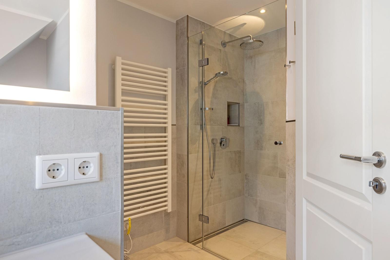 Dusche mit Glaswand, Heizkörper und Steckdosen an der Wand