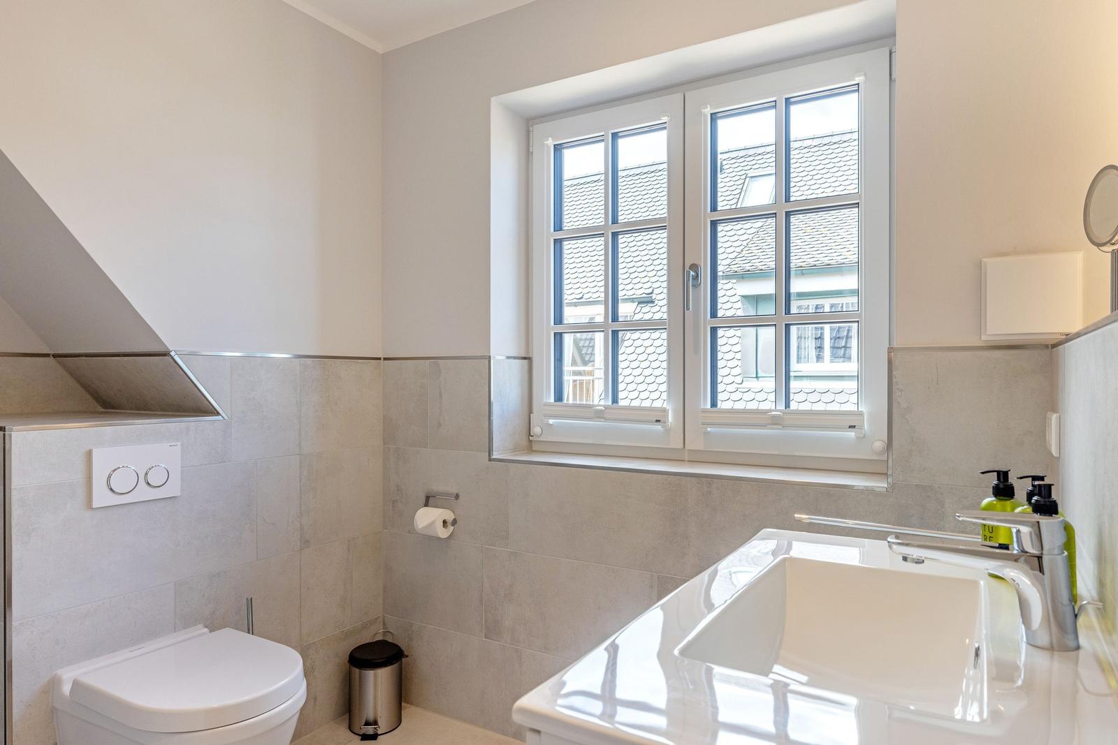 Badezimmer mit Toilette, Waschbecken und Fenster.