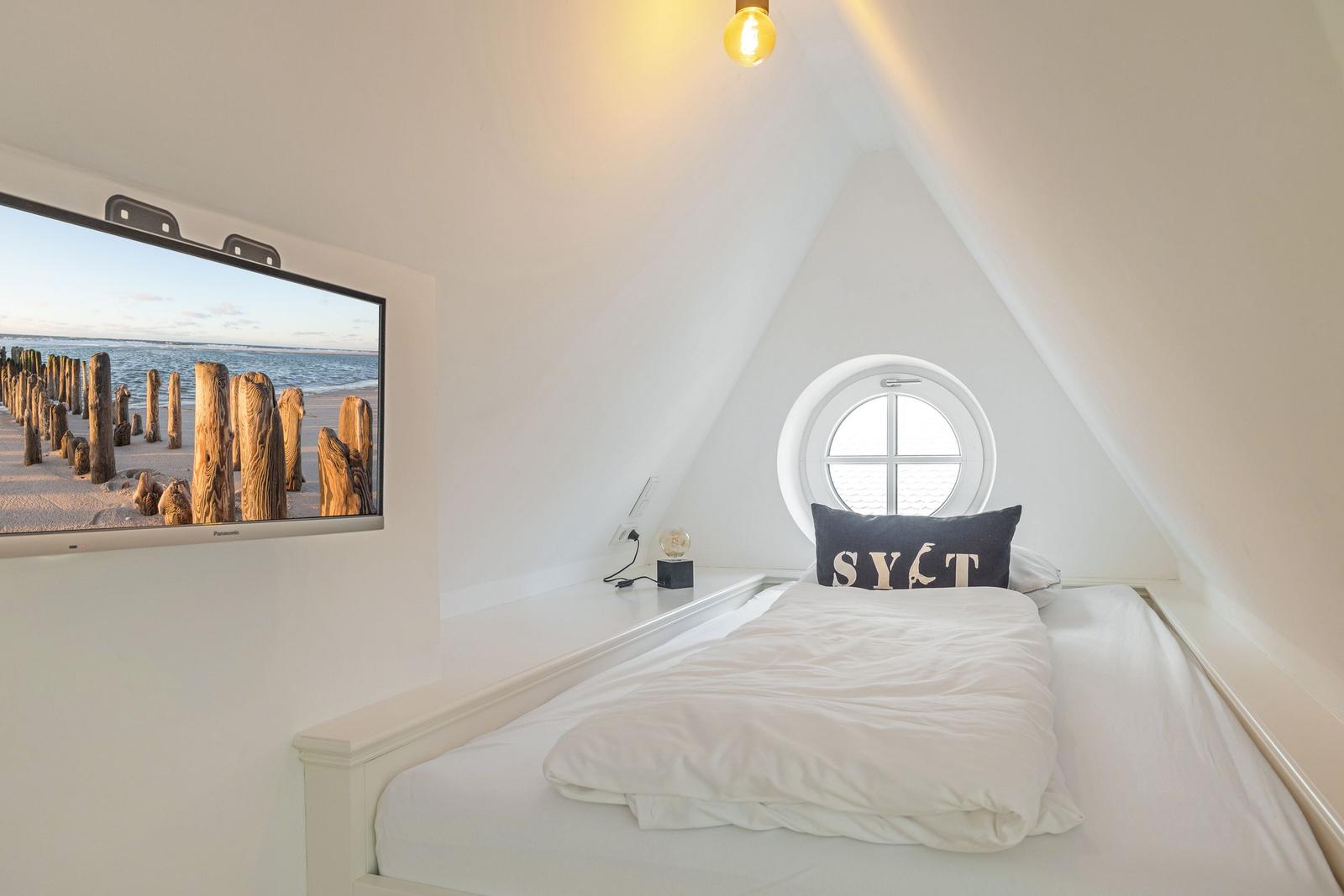 Schlafzimmer mit Dachschrägen, Rundfenster und Wandbildschirm