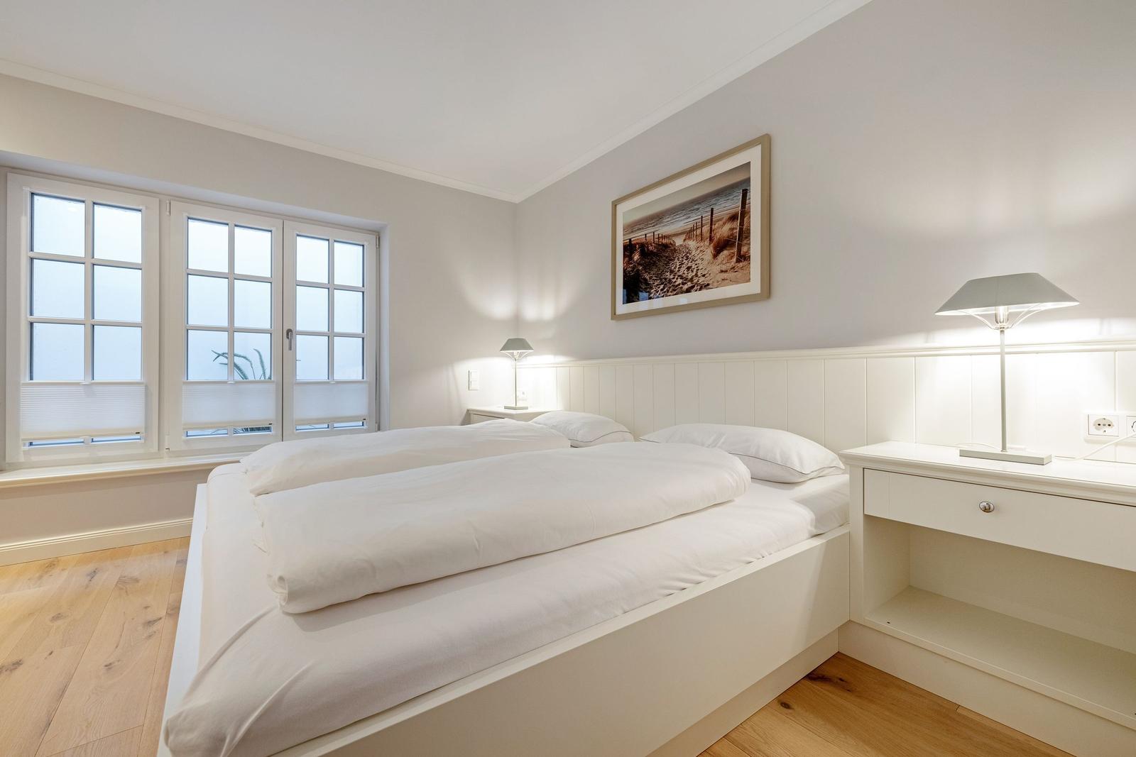 Schlafzimmer mit Doppelbett, Fenster und Nachttisch.