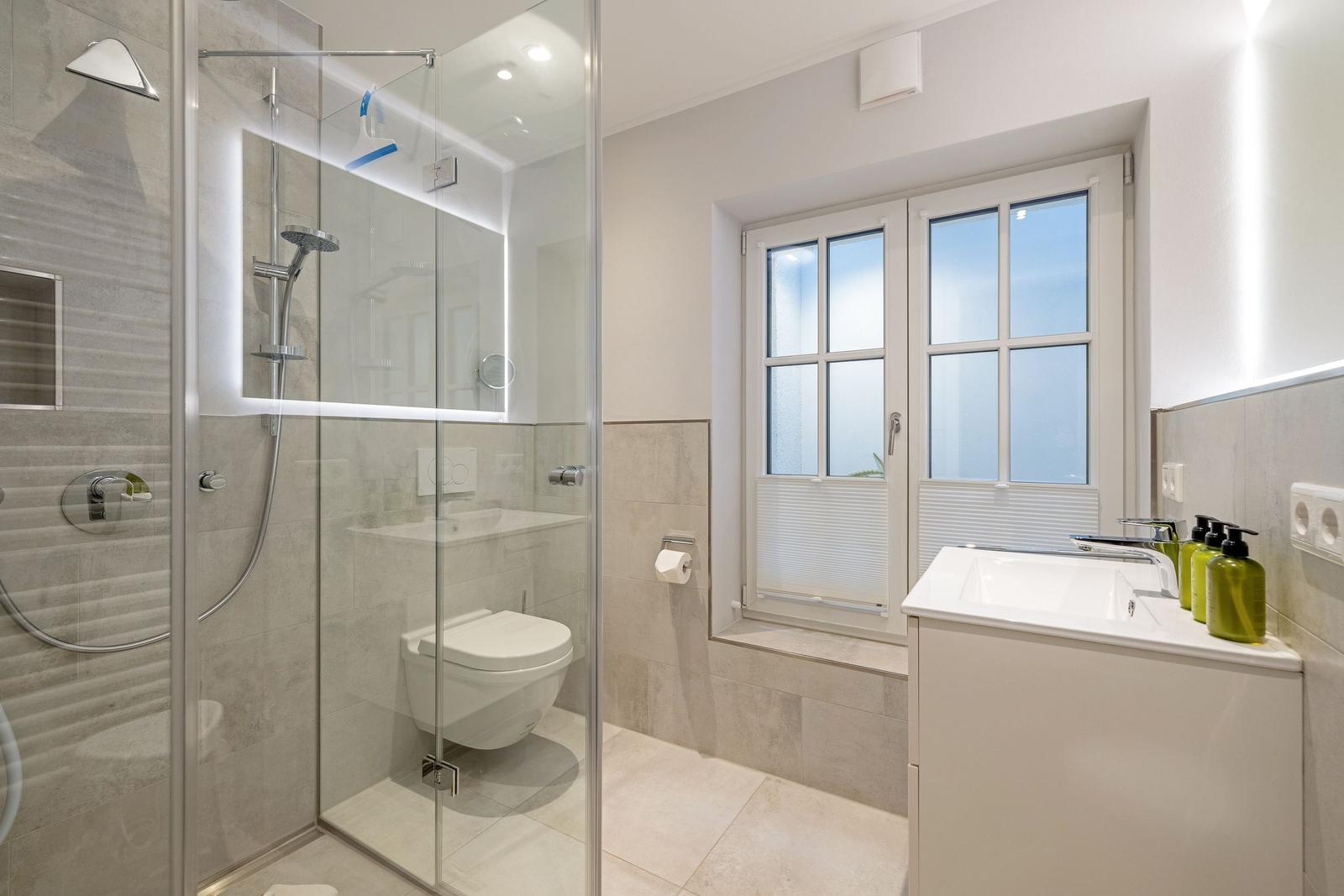 Bad mit Dusche, WC und Waschbecken. Fenster mit Jalousie.