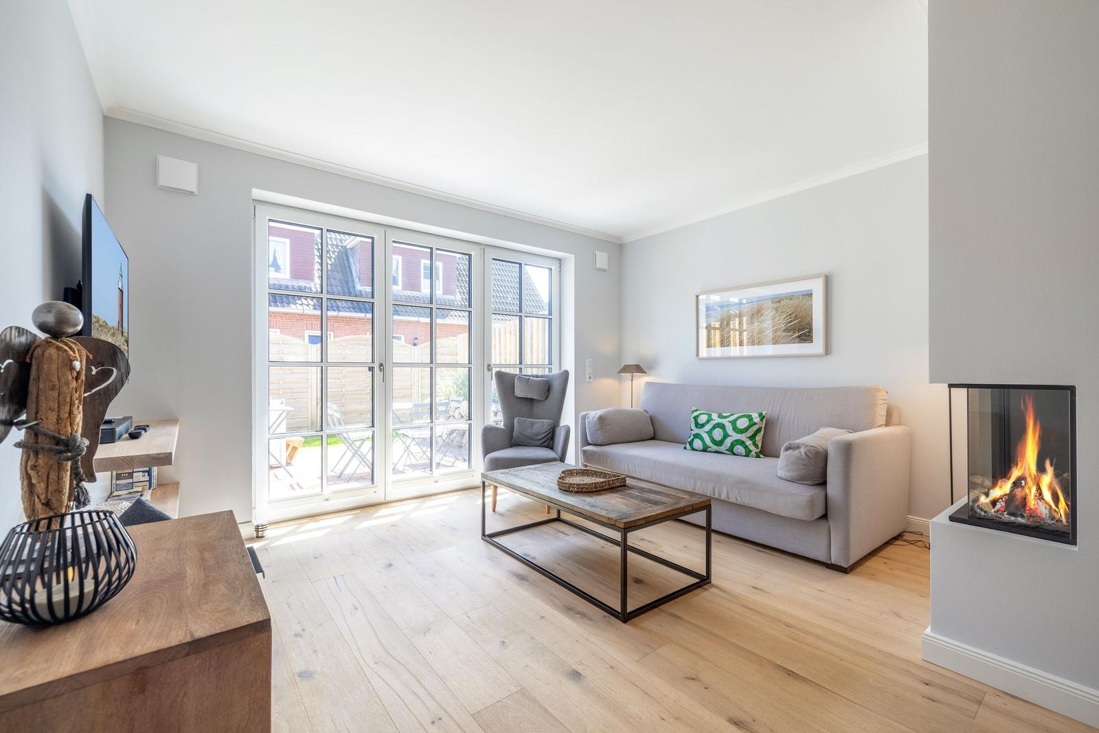 Wohnzimmer mit Sofa, Kamin und Glastür zum Garten.