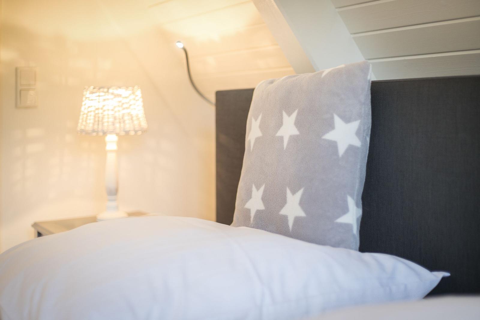 Schlafzimmer mit Bett, Kissen und Nachttischlampe unter Dachschrägen.