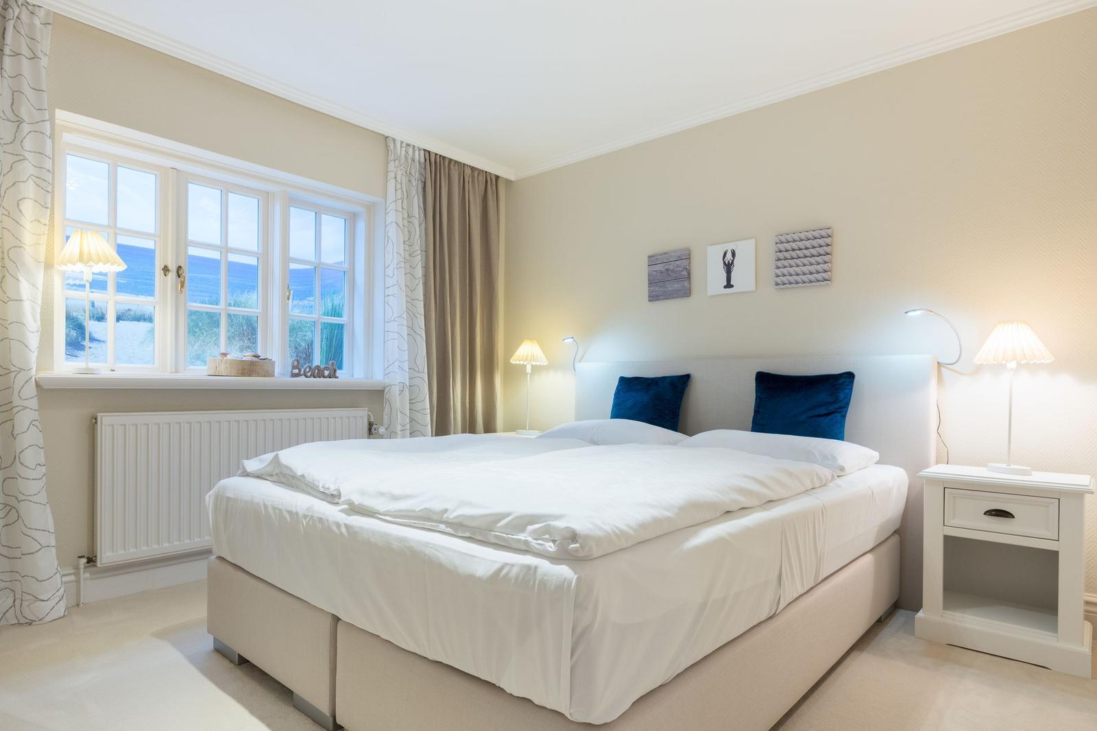 Schlafzimmer mit Doppelbett, Fenster mit Meerblick und Nachttischen mit Lampen.