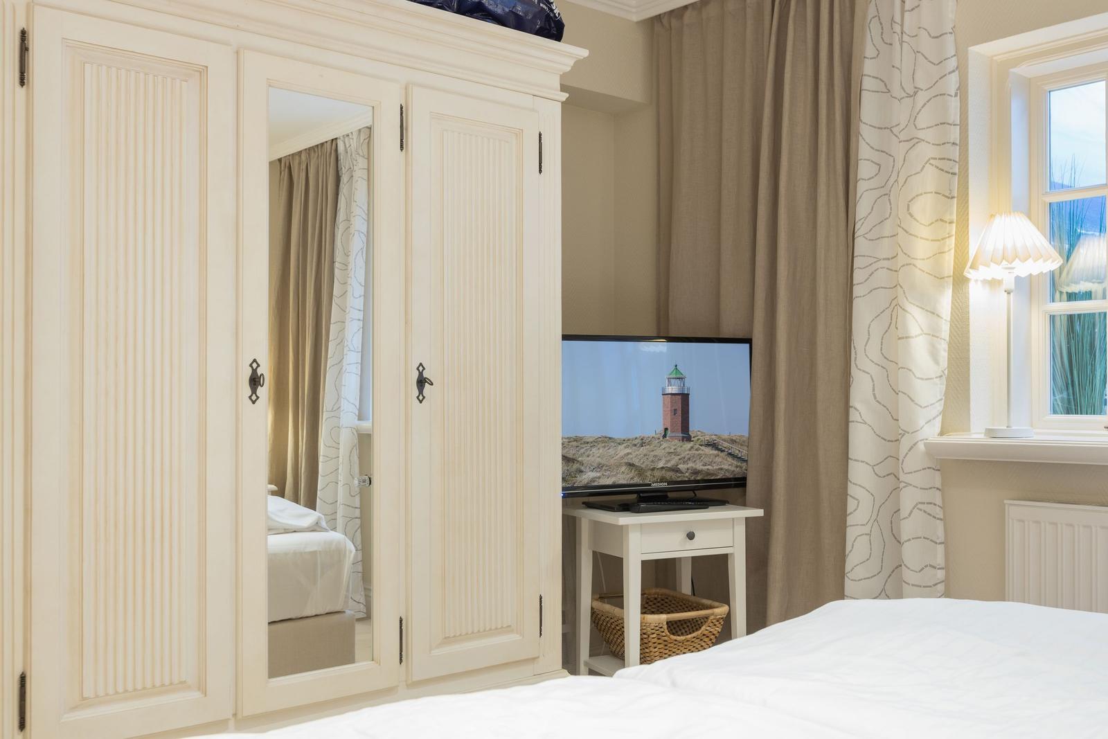 Schlafzimmer mit Kleiderschrank, Fernseher und Fenster mit Vorhängen.