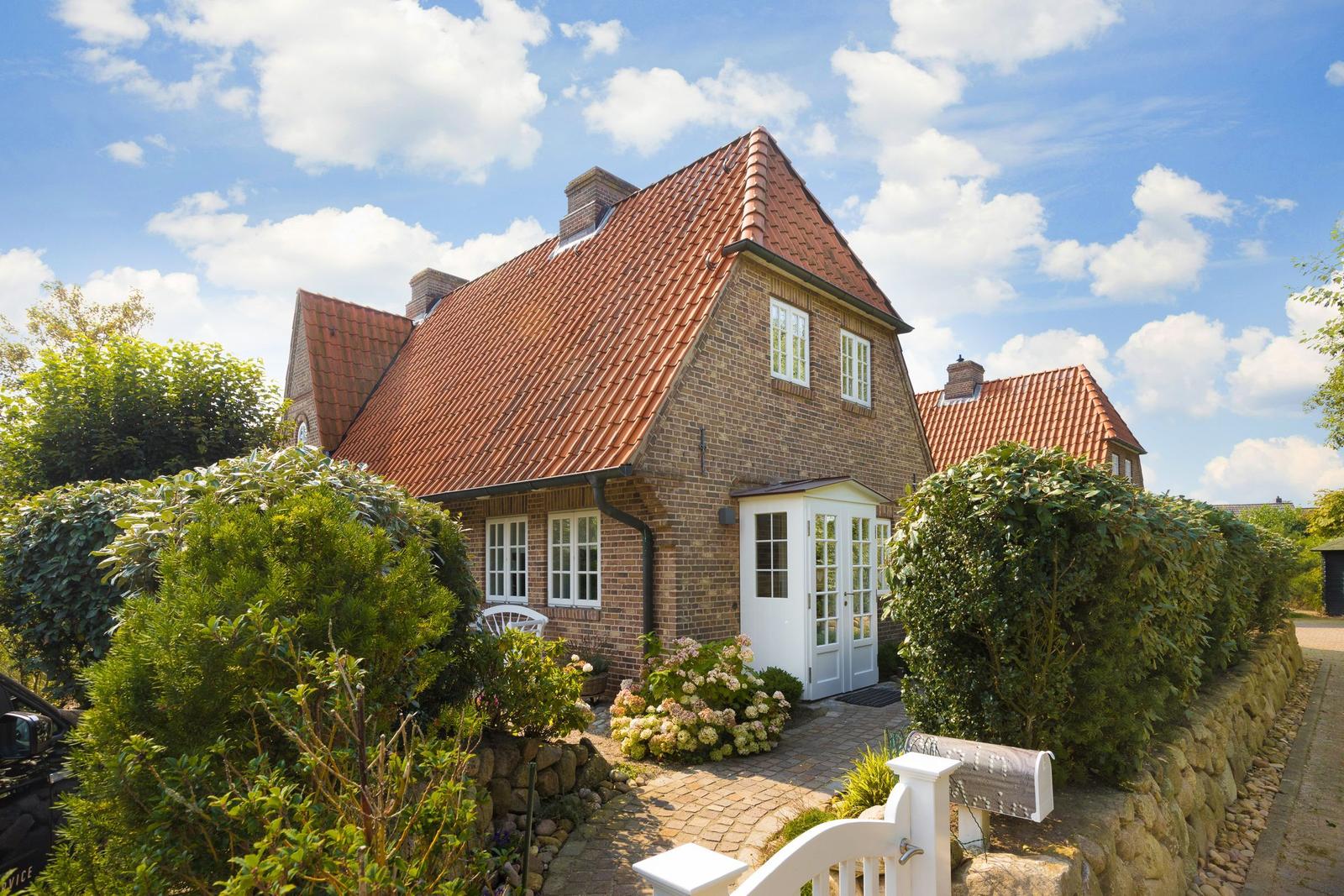 Ein Haus mit rotem Ziegeldach, weißer Tür und umliegenden grünen Sträuchern.
