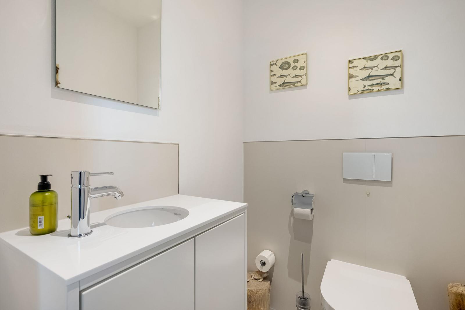 Badezimmer mit Waschbecken, Spiegel und Toilette. Wandbilder zeigen Fische.