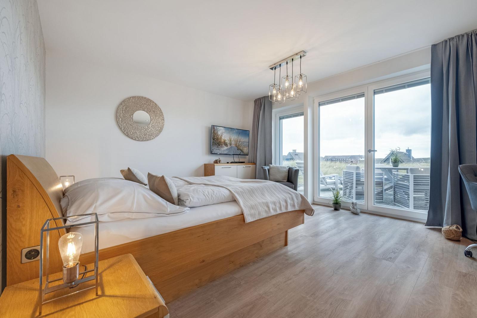 Schlafzimmer mit Bett, Fernseher und Balkonansicht.