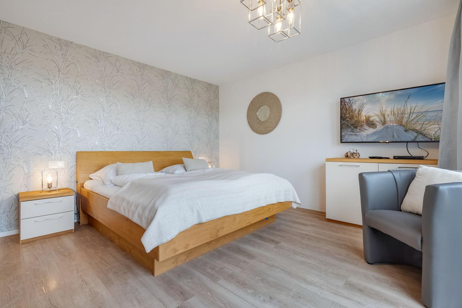 Schlafzimmer mit Bett, Nachttisch, Fernseher und Sessel.
