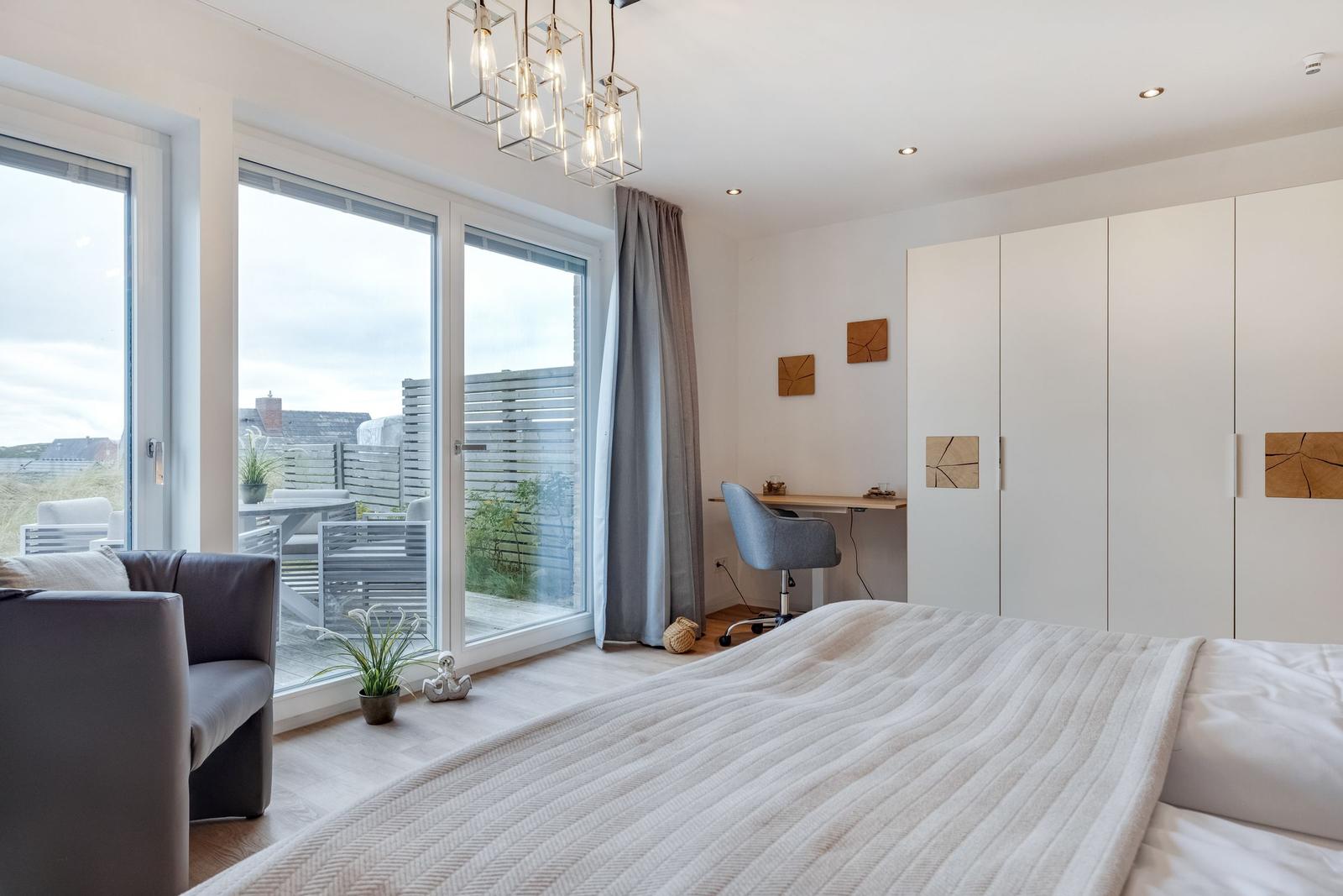 Schlafzimmer mit Bett, Schreibtisch und Balkonansicht.