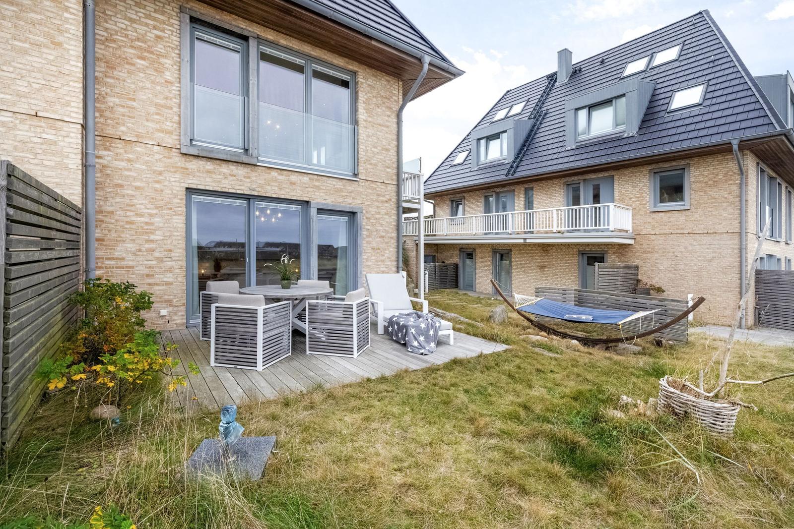 Terrasse mit Sitzgruppe und Hängematte im Garten. Modernes Haus mit Holzfassade.