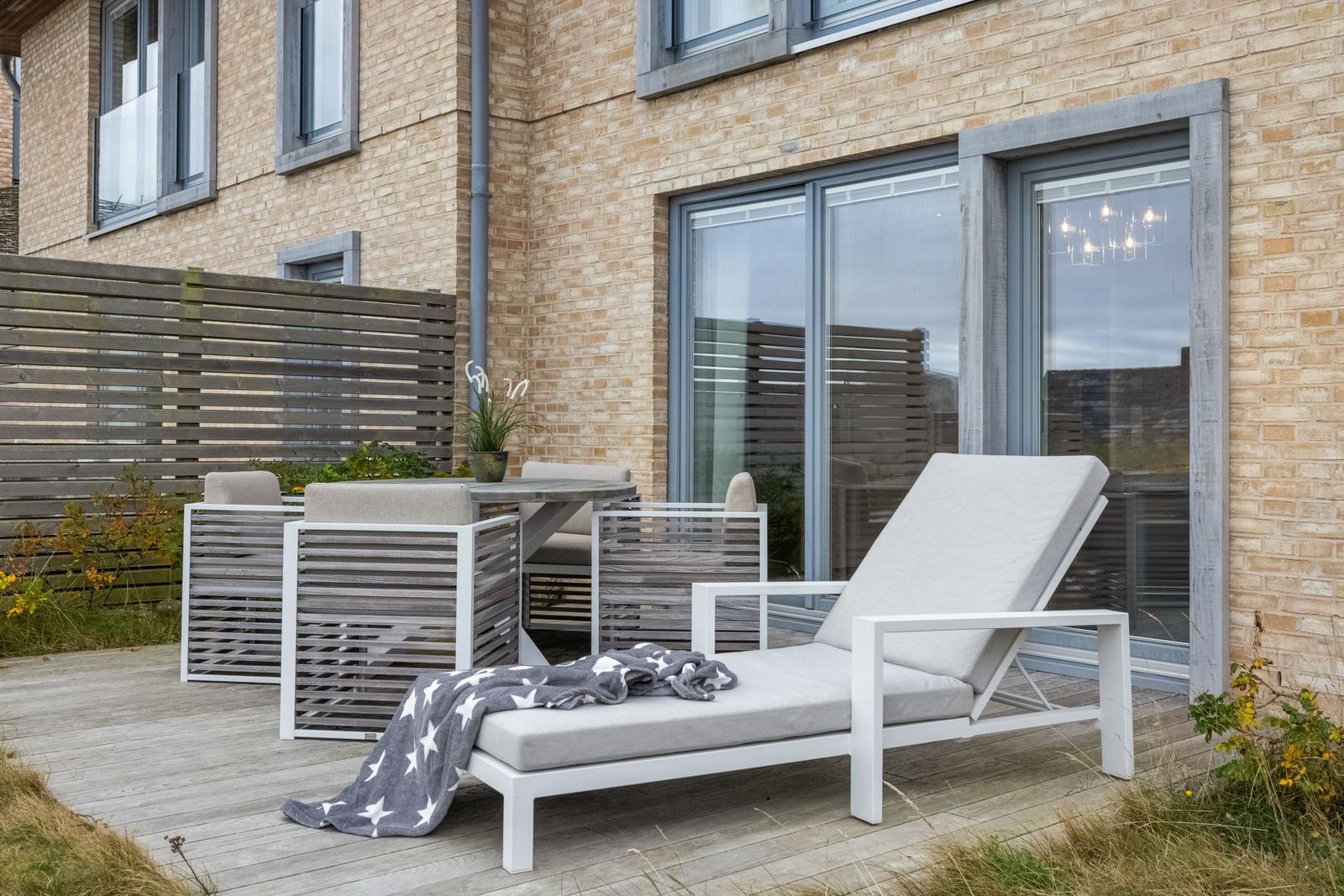 Terrasse mit Loungemöbeln und Tisch. Holzfußboden und Backsteinhaus im Hintergrund.