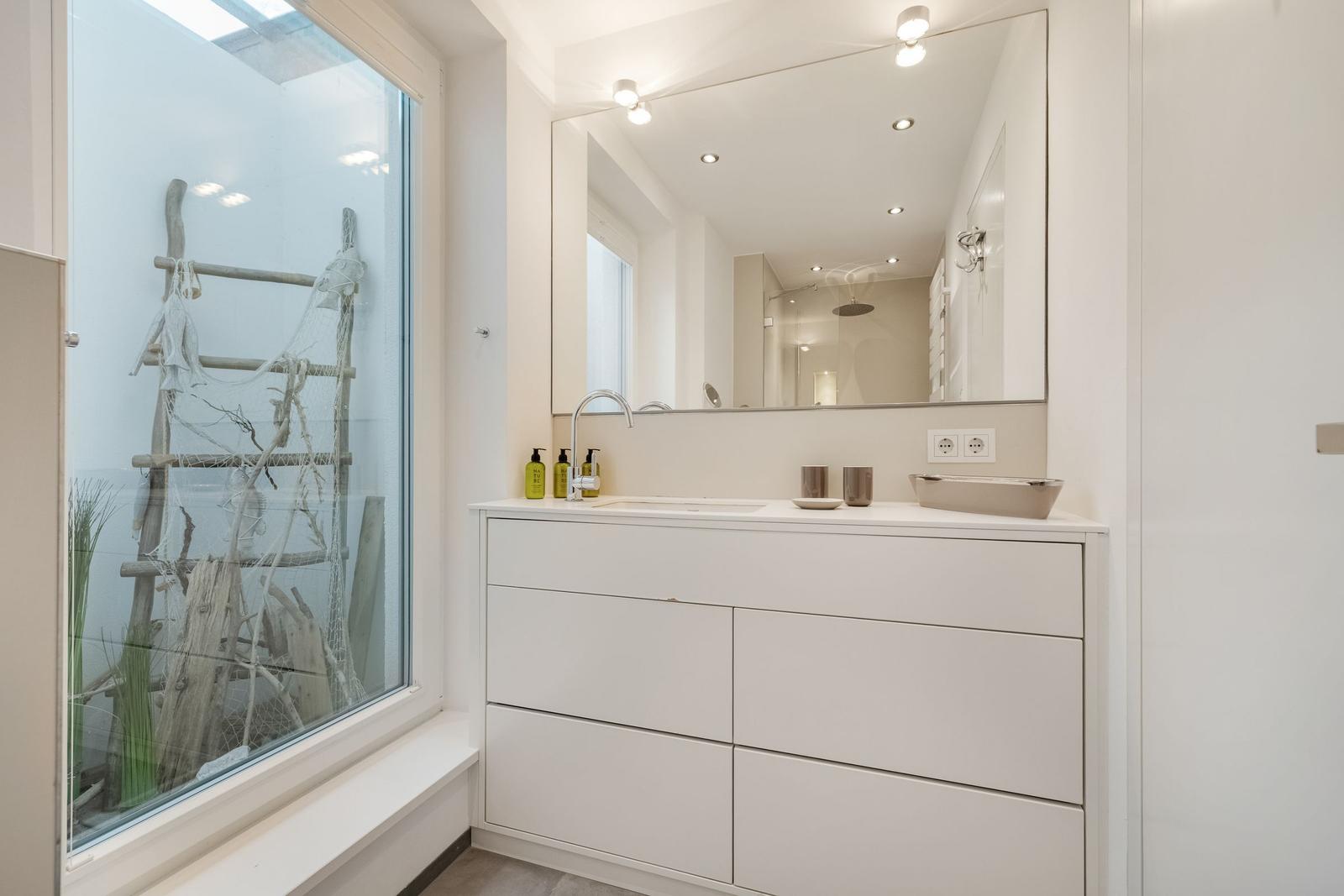 Badezimmer mit Waschtisch, Spiegel und großem Fenster zur Außenseite.