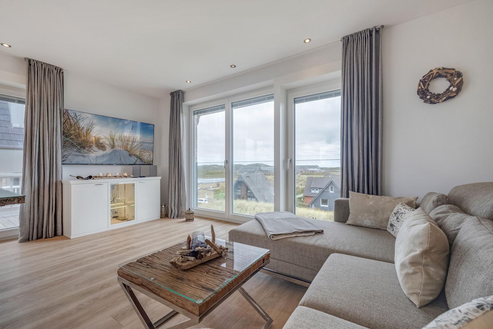 Wohnzimmer mit Sofa, Glas-Tisch und Blick auf die Landschaft.