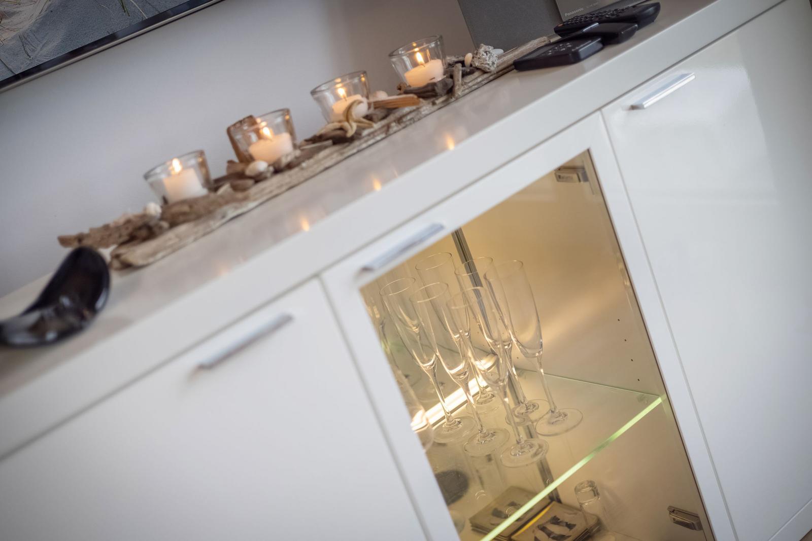 Weißer Schrank mit Gläsern und Kerzen auf der Oberfläche.