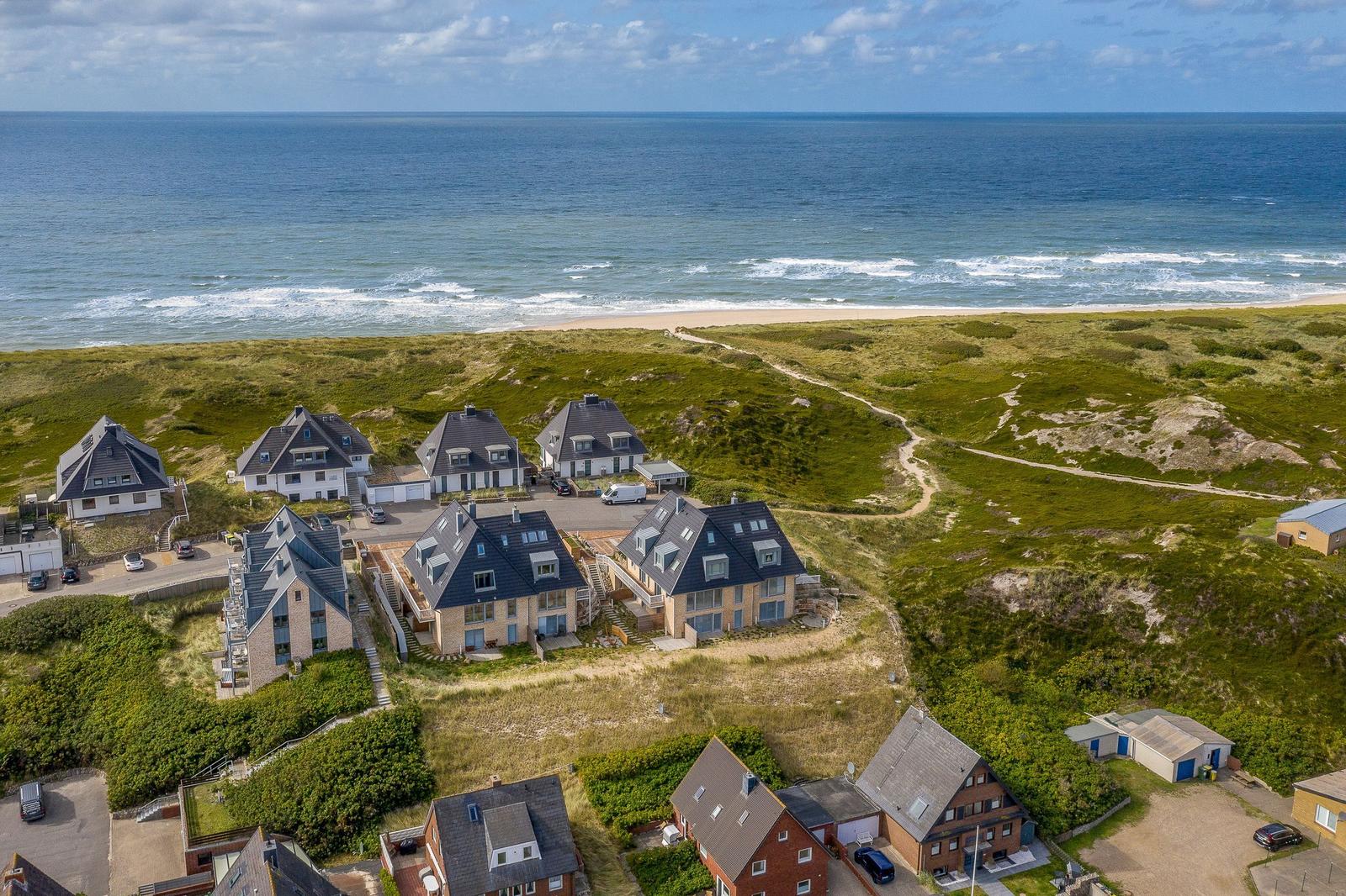 Meerfront-Villen auf grünen Dünen mit Blick auf den Strand.
