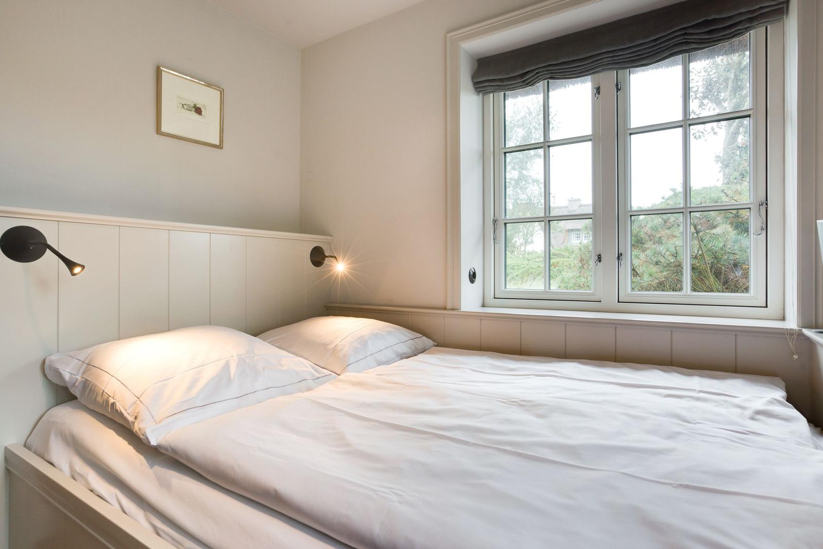 Schlafzimmer mit Bett, Fenster und Wandlampen.