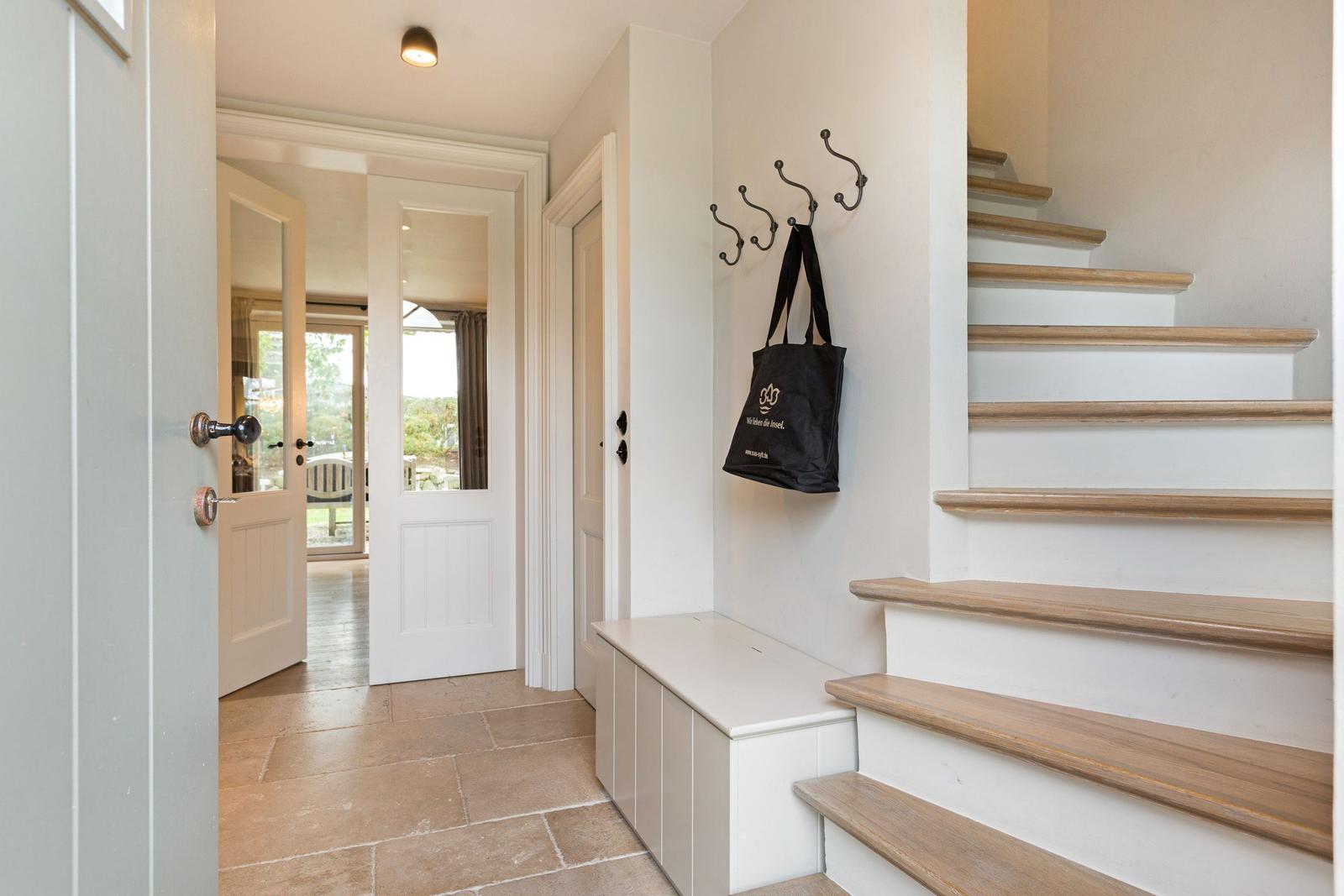 Eingangsbereich mit Treppe und Hakenwand. Schwarze Tasche hängt an der Wand.