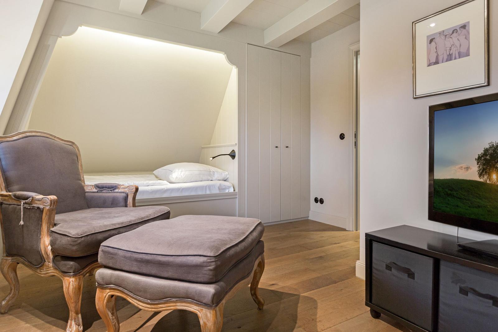 Schlafzimmer mit Bett, Stuhl und Fernseher an der Wand.