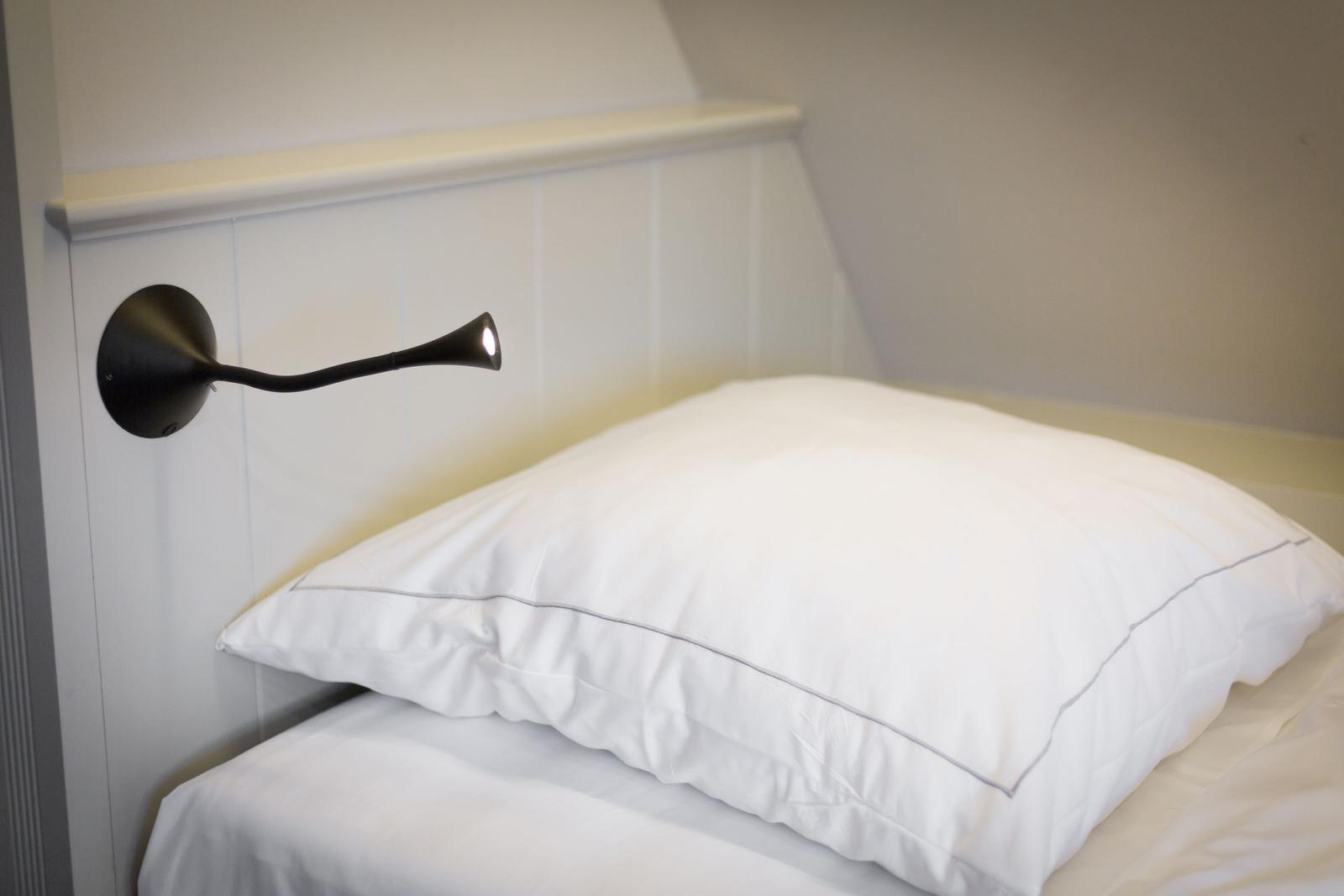 Schlafzimmer mit weißem Bett und Wandlampe.