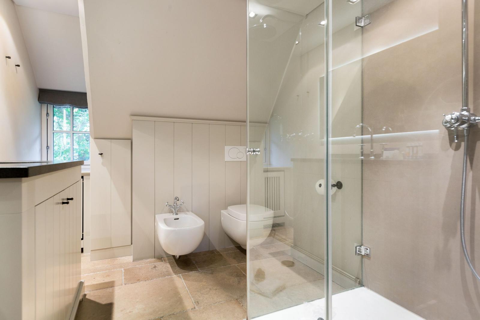 Badezimmer mit Dusche, Toilette und Bidet. Holzwand und Steinboden.